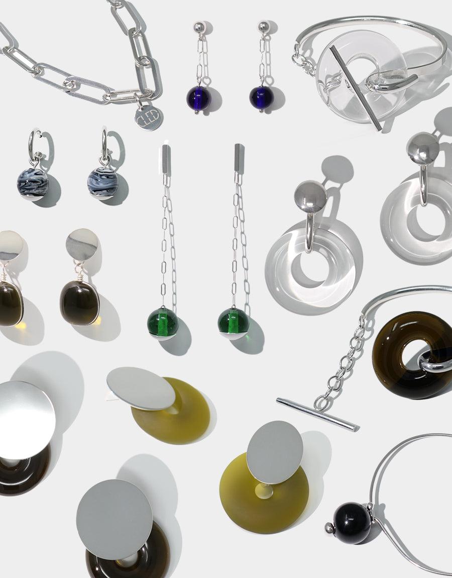 A collection of unique earrings and bracelet crafted from upcycled glass, showcasing CLED's commitment to environmentally conscious jewelry design and local production.