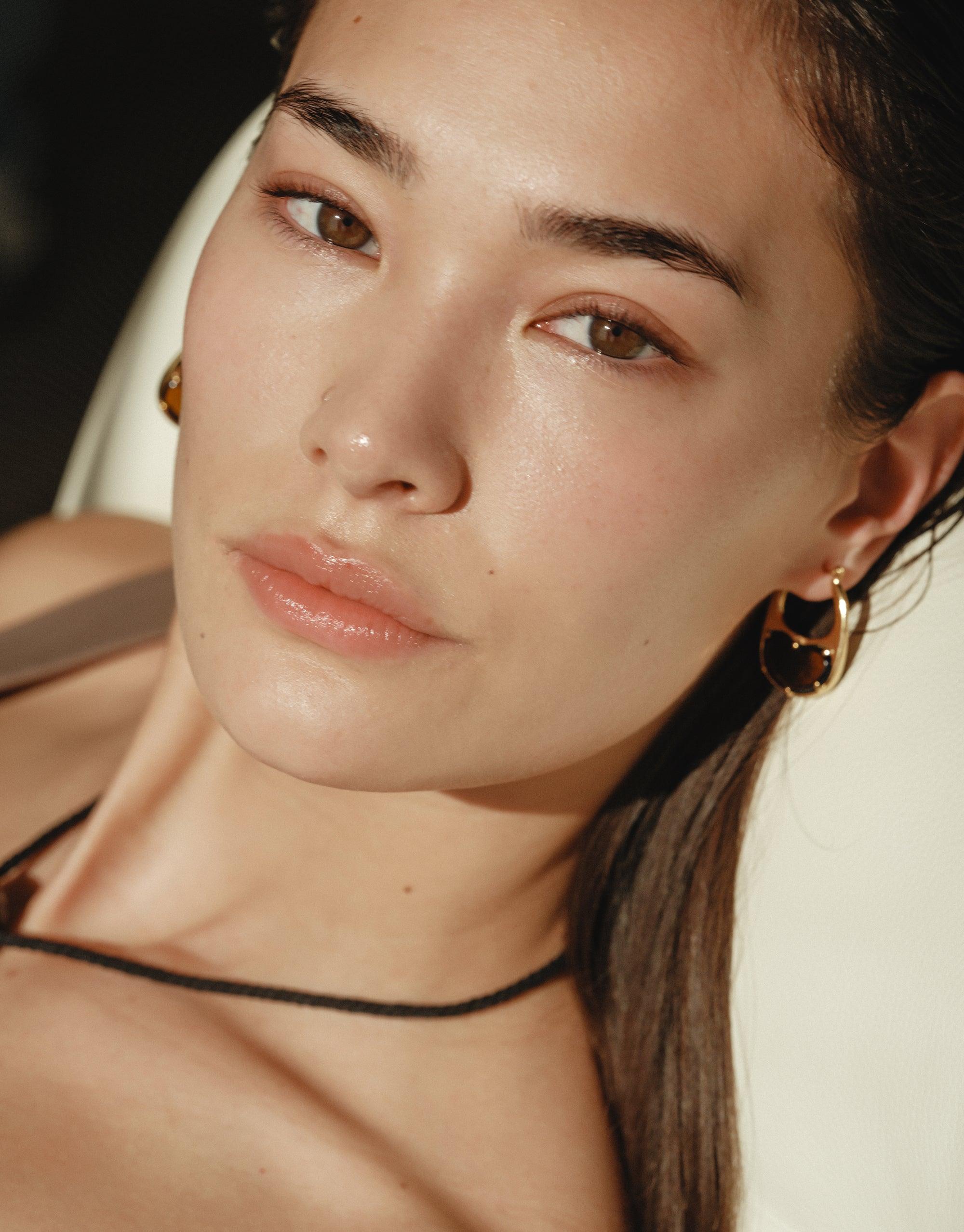 Close-up portrait showcasing Bean Hoop Earrings | Large, featuring elegant gold hoops with a unique bean-inspired design. The earrings complement the model's natural beauty, highlighting the organic shapes and curves inspired by nature's creativity. CLED