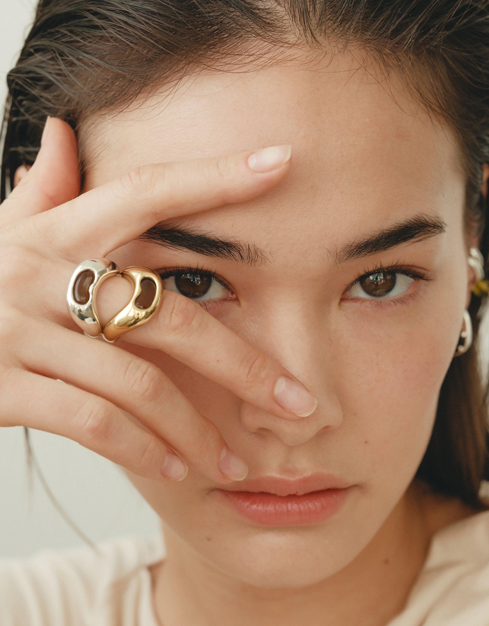Close-up of a model wearing the Bean Ring, showcasing its unique organic shape inspired by legume plants. The ring's curved design elegantly frames the model's eye, highlighting the jewelry's natural beauty and transformative energy. Bean Ring by CLED.