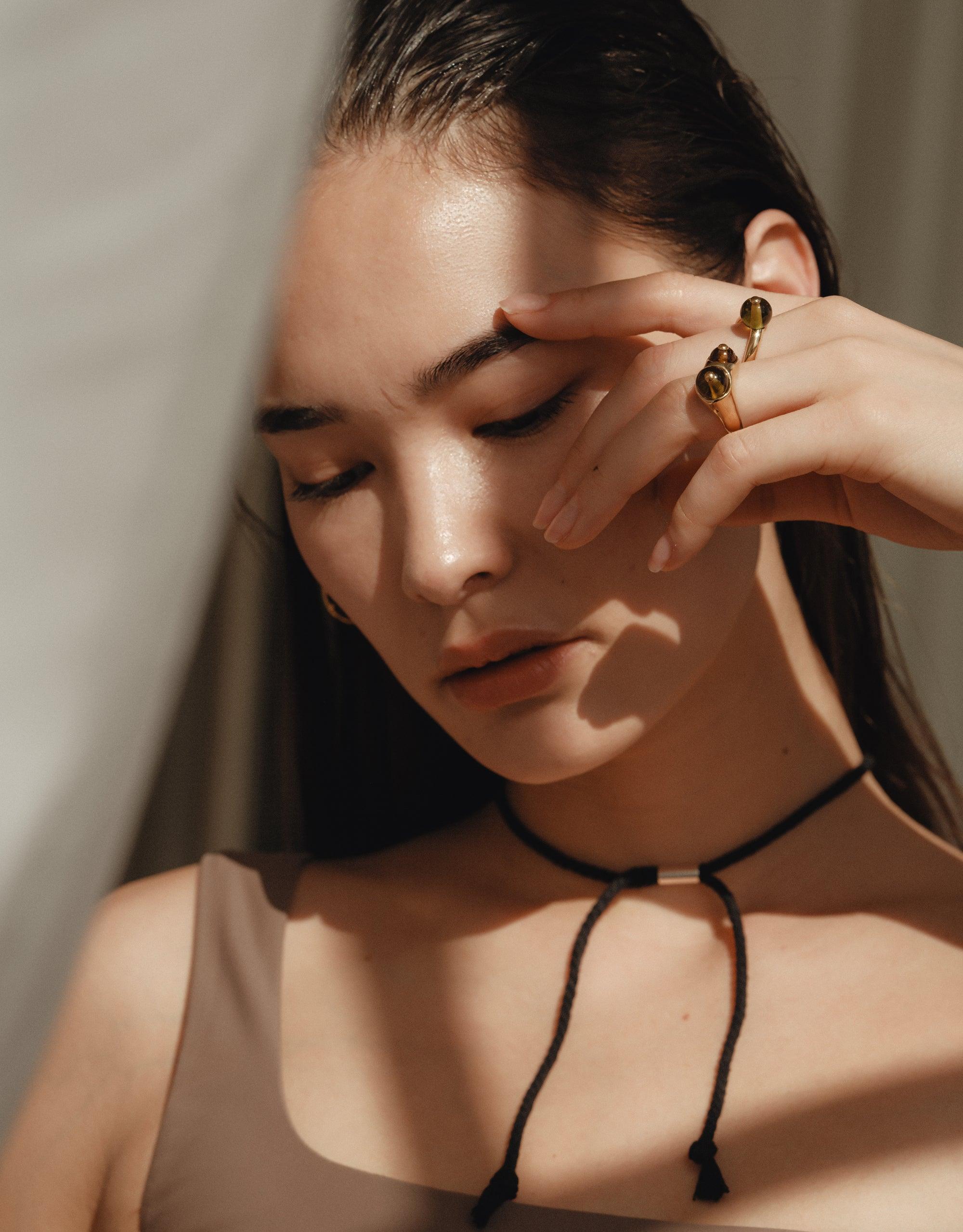 Close-up of a person wearing a sleek black choker necklace and unique ring, showcasing the elegant Black Pea Necklace. The jewelry complements the model's natural beauty, capturing the organic, transformative essence of CLED's design philosophy.