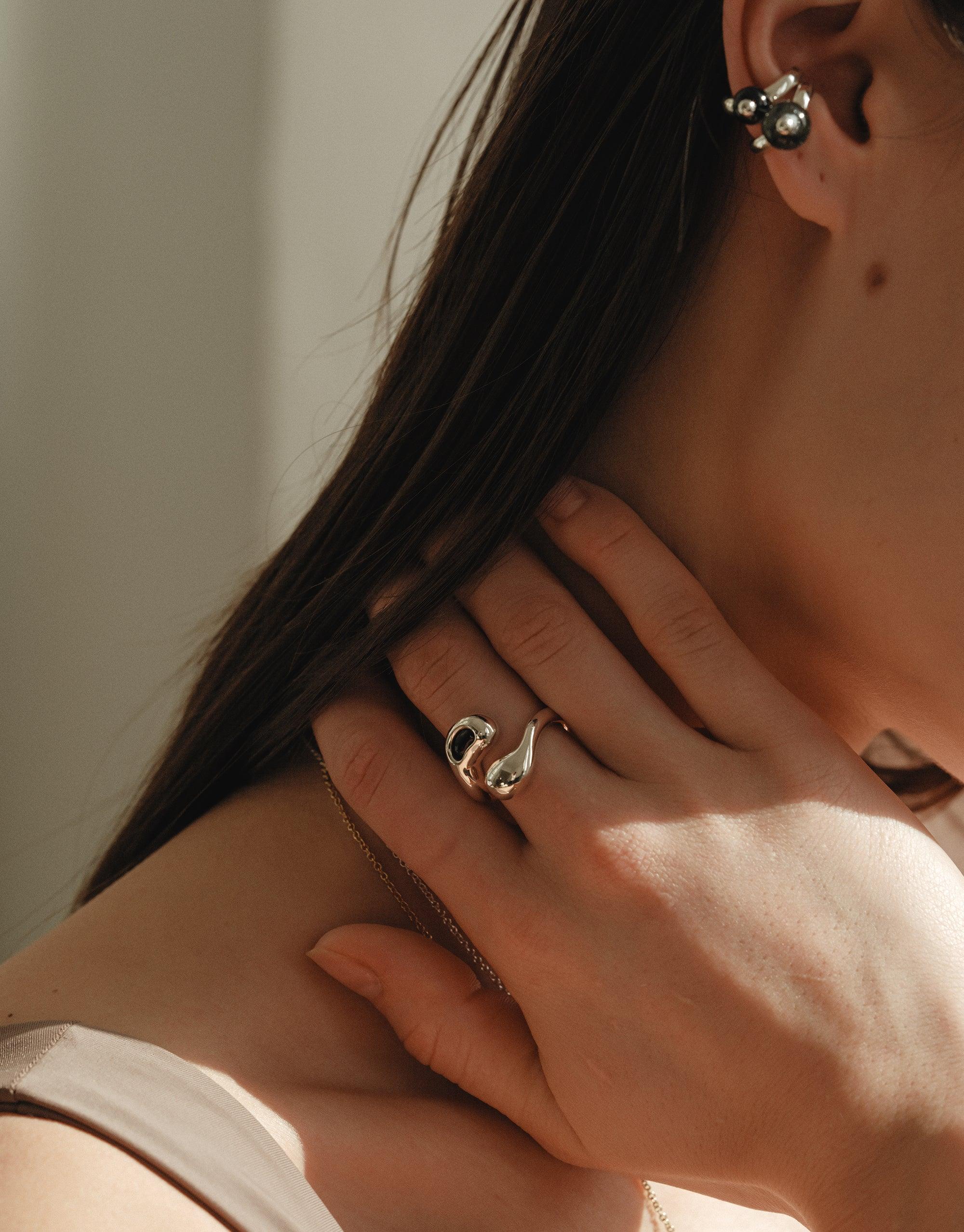 Close-up of a woman wearing small pear ear cuffs inspired by legume shapes and wearing the sprout ring in black stone
