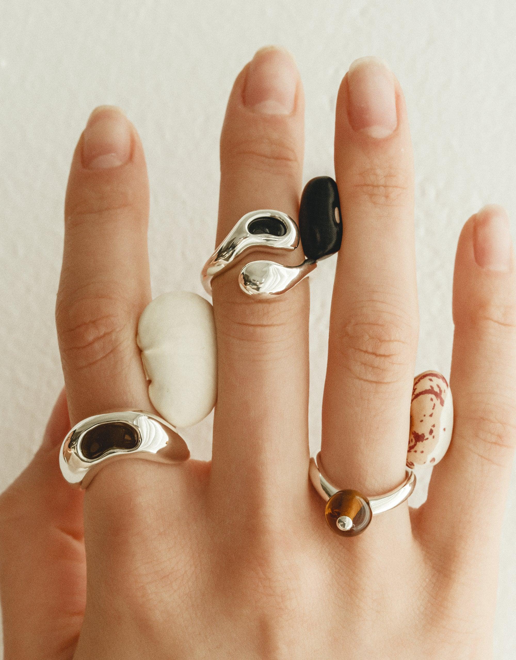 Sculptural silver and organic-shaped rings inspired by legumes, showcasing nature's creativity. Bean Ring collection features unique designs with smooth curves and contrasting elements, worn on multiple fingers. Sustainable jewelry by CLED