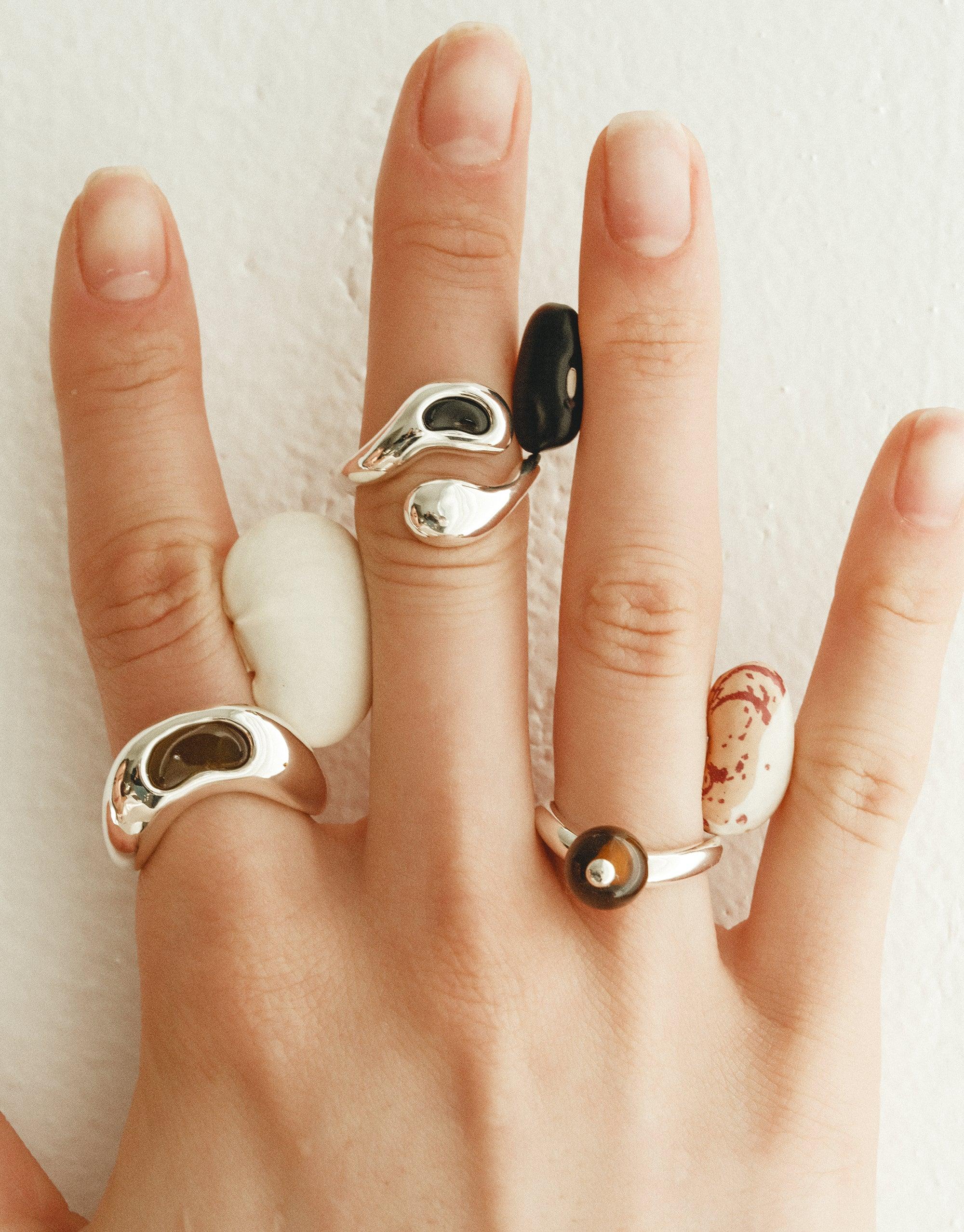 Sculptural silver and organic-shaped rings inspired by legumes, showcasing nature's creativity. Bean Ring collection features unique designs with smooth curves and contrasting elements, worn on multiple fingers. Sustainable jewelry capturing the essence of growth and transformation. CLED Bean Ring