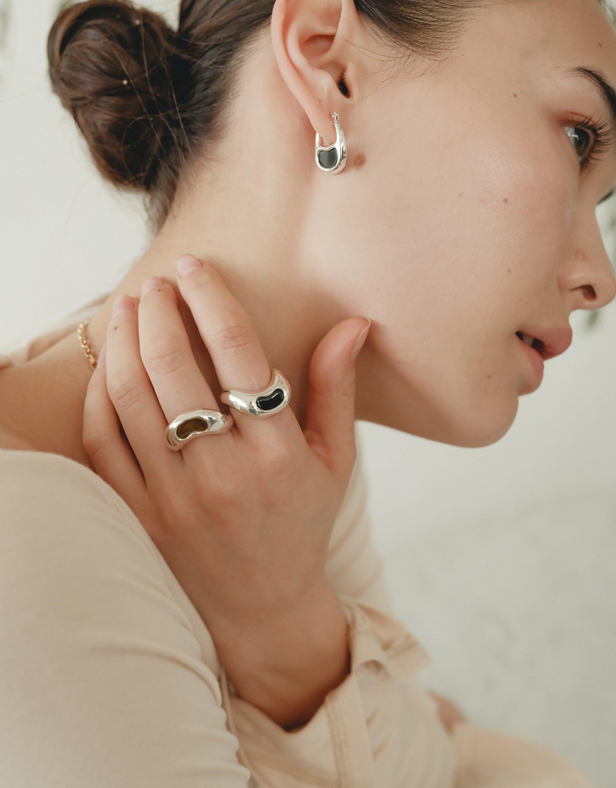Elegant model showcasing Bean Ring jewelry, featuring organic shapes inspired by legumes. Silver earrings and rings with curved designs, reflecting nature's beauty. Soft profile view emphasizes the delicate and transformative essence of the collection. Bean Ring by CLED