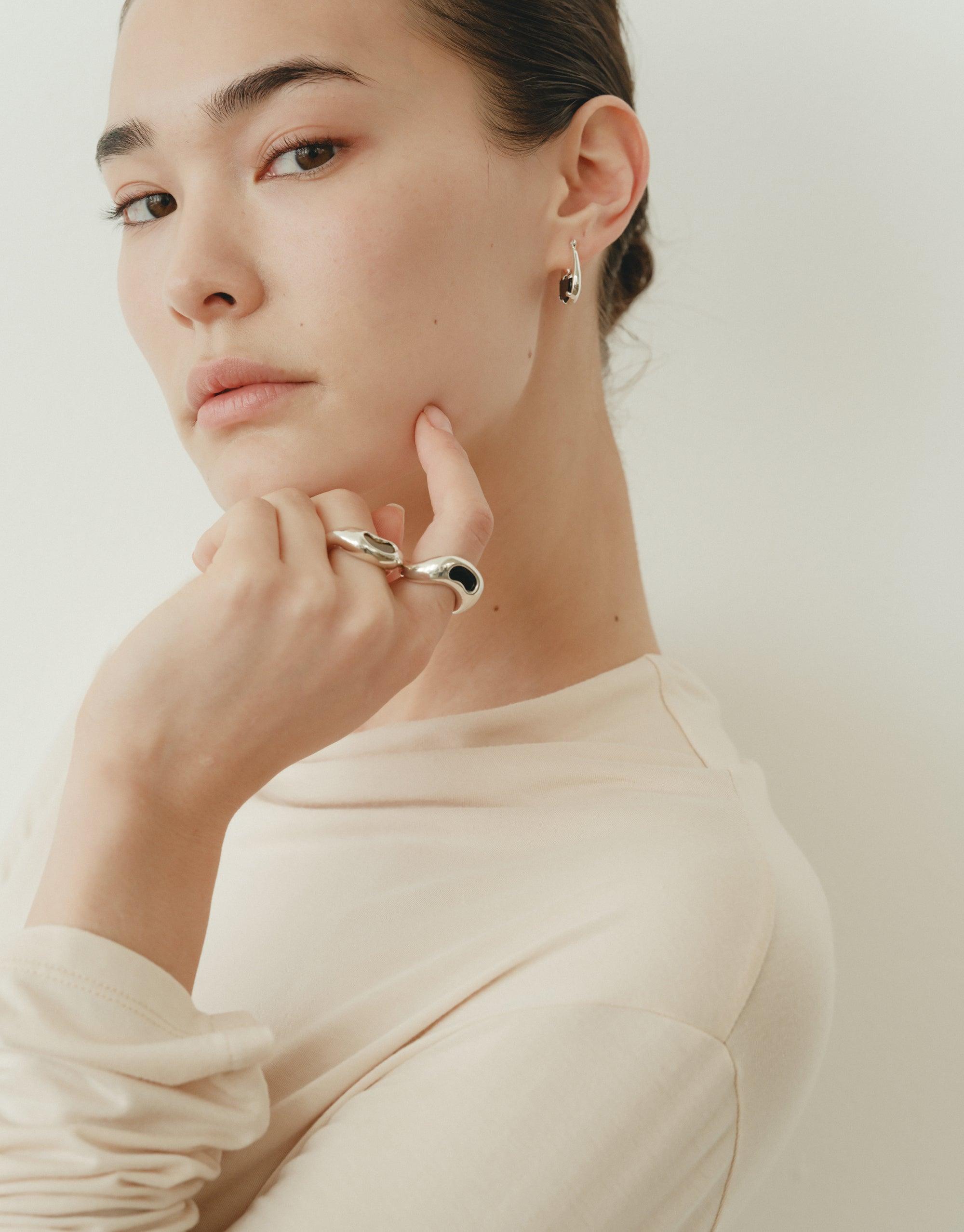 Elegant model showcasing the Bean Ring, a nature-inspired silver jewelry piece with organic curves reminiscent of legume patterns. The ring's unique design captures the essence of growth and transformation, beautifully complementing the model's neutral attire and thoughtful pose. CLED Bean Ring
