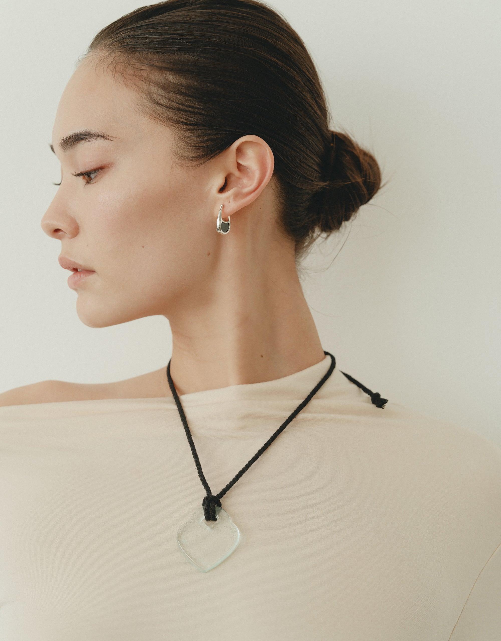 Profile view of a woman wearing a Clear Heart Necklace, showcasing the organic shape inspired by nature's creativity. The necklace features a transparent heart pendant on a black cord, reflecting the collection's theme of growth and transformation. CLED Clear Heart Necklace.