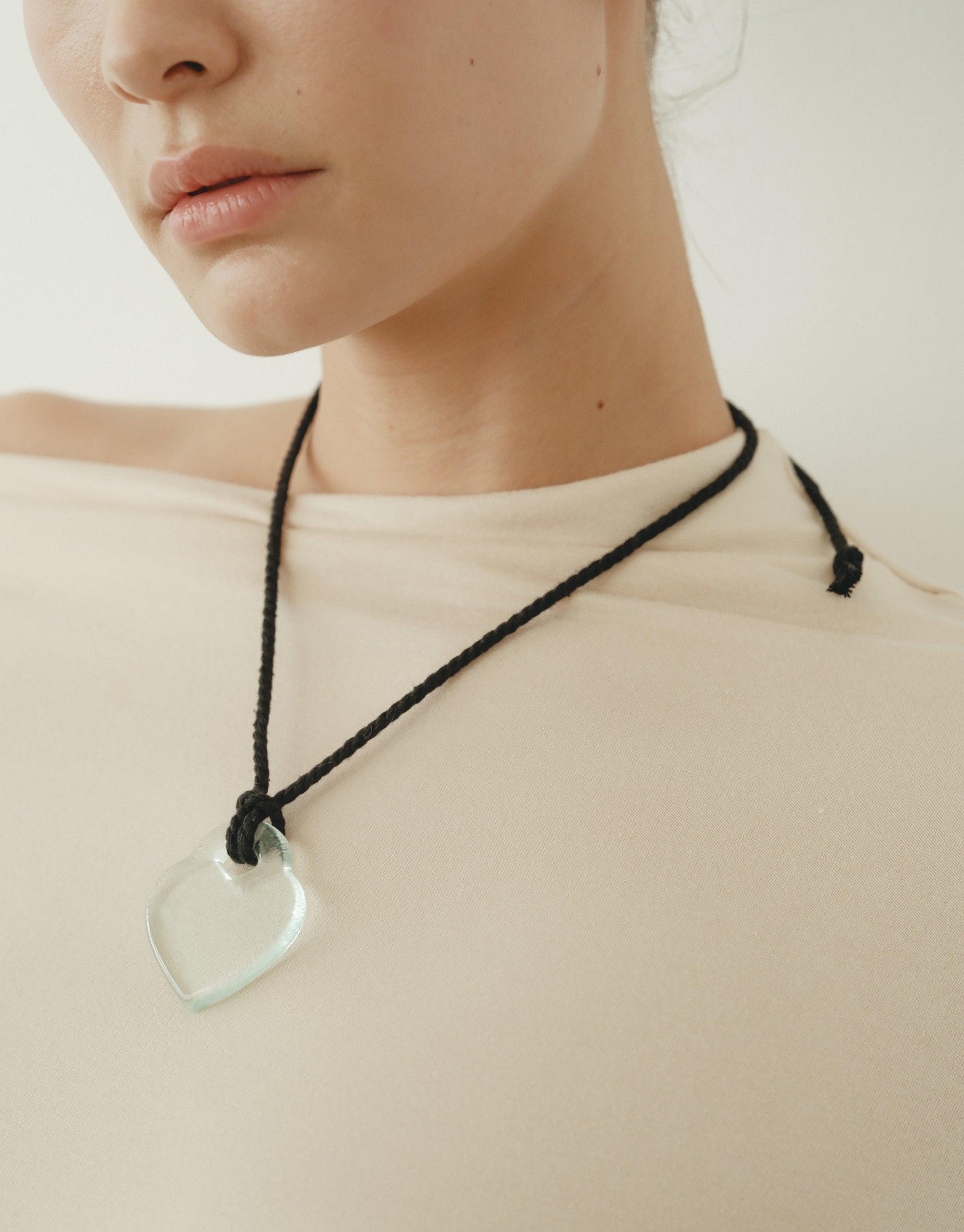 Elegant Clear Heart Necklace with black cord, inspired by nature's organic shapes and transformative energy. Minimalist design showcases delicate heart pendant against neutral background. Perfect accessory for a subtle, sophisticated look. Clear Heart Necklace by CLED