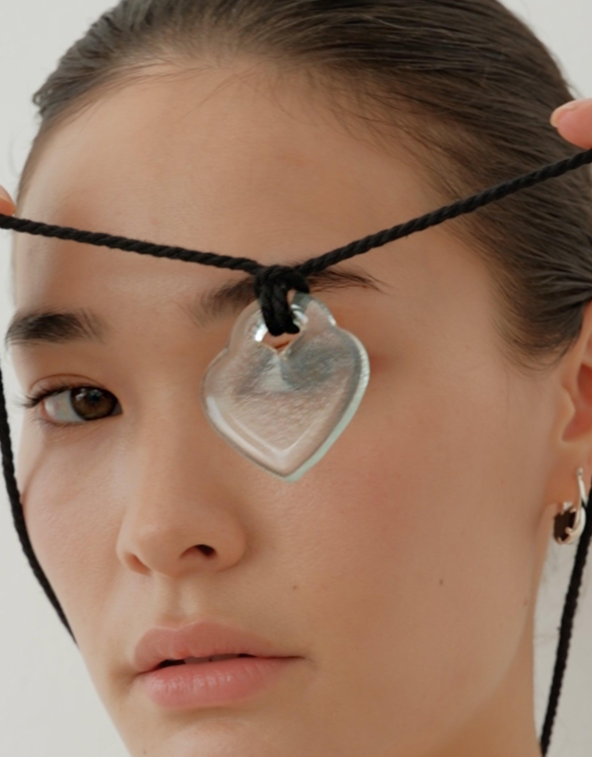 Close-up view of Clear Heart Necklace, featuring a transparent heart-shaped pendant on a black cord, showcasing its elegant design inspired by nature's organic shapes and patterns. A unique piece that captures the essence of growth and transformation. CLED, Clear Heart Necklace.