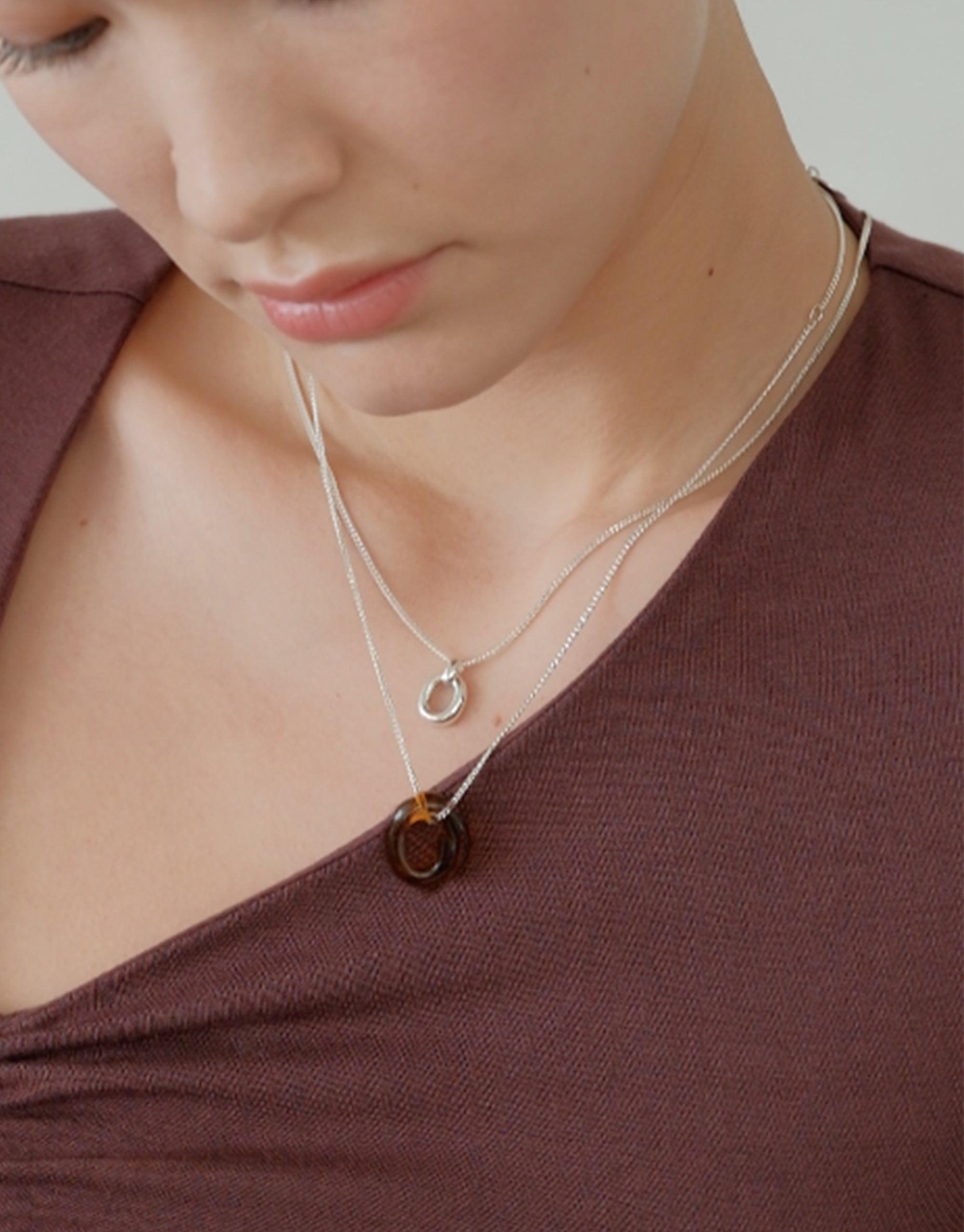Delicate silver necklace featuring a small core loop pendant, worn layered with an amber-colored pendant. The Small Core Loop Necklace showcases minimalist design and sustainable craftsmanship, symbolizing unity and connection. Perfect for everyday wear or special occasions. CLED Small Core Loop Necklace.