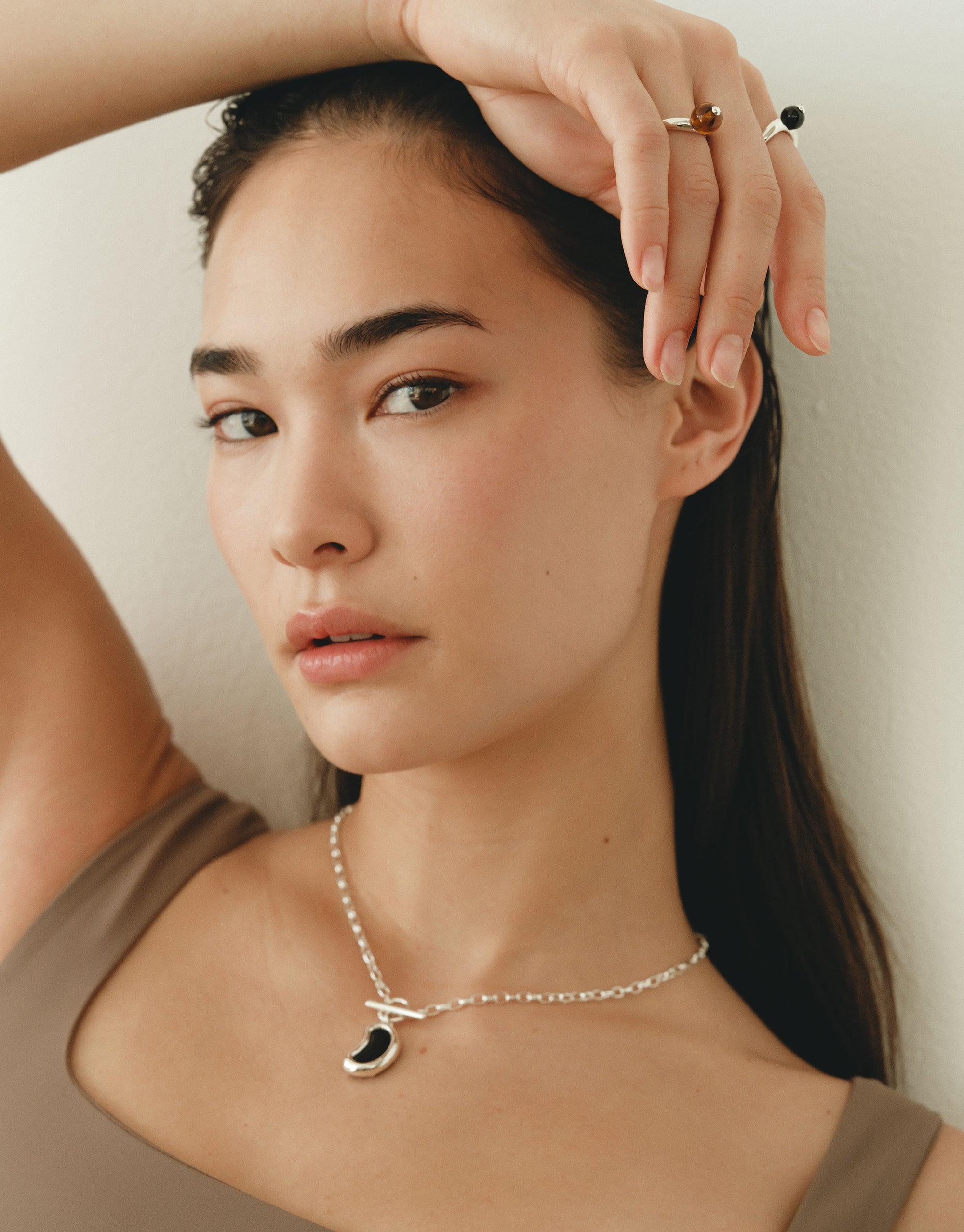 Elegant model wearing Bean Toggle Necklace, showcasing organic shape inspired by nature's creativity. Delicate silver chain with unique bean-shaped pendant, capturing essence of growth and transformation. Perfect accessory for nature-inspired style. Bean Toggle Necklace by CLED.