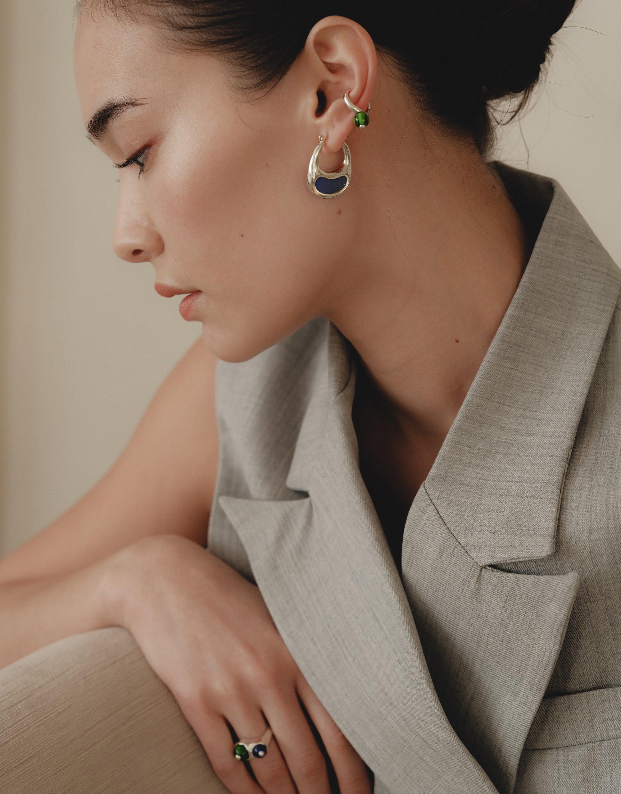 Side profile of a person wearing Bean Hoop Earrings | Large, showcasing the elegant curve and organic shape inspired by nature. The earrings complement a sophisticated light-colored blazer, embodying growth and transformation. CLED