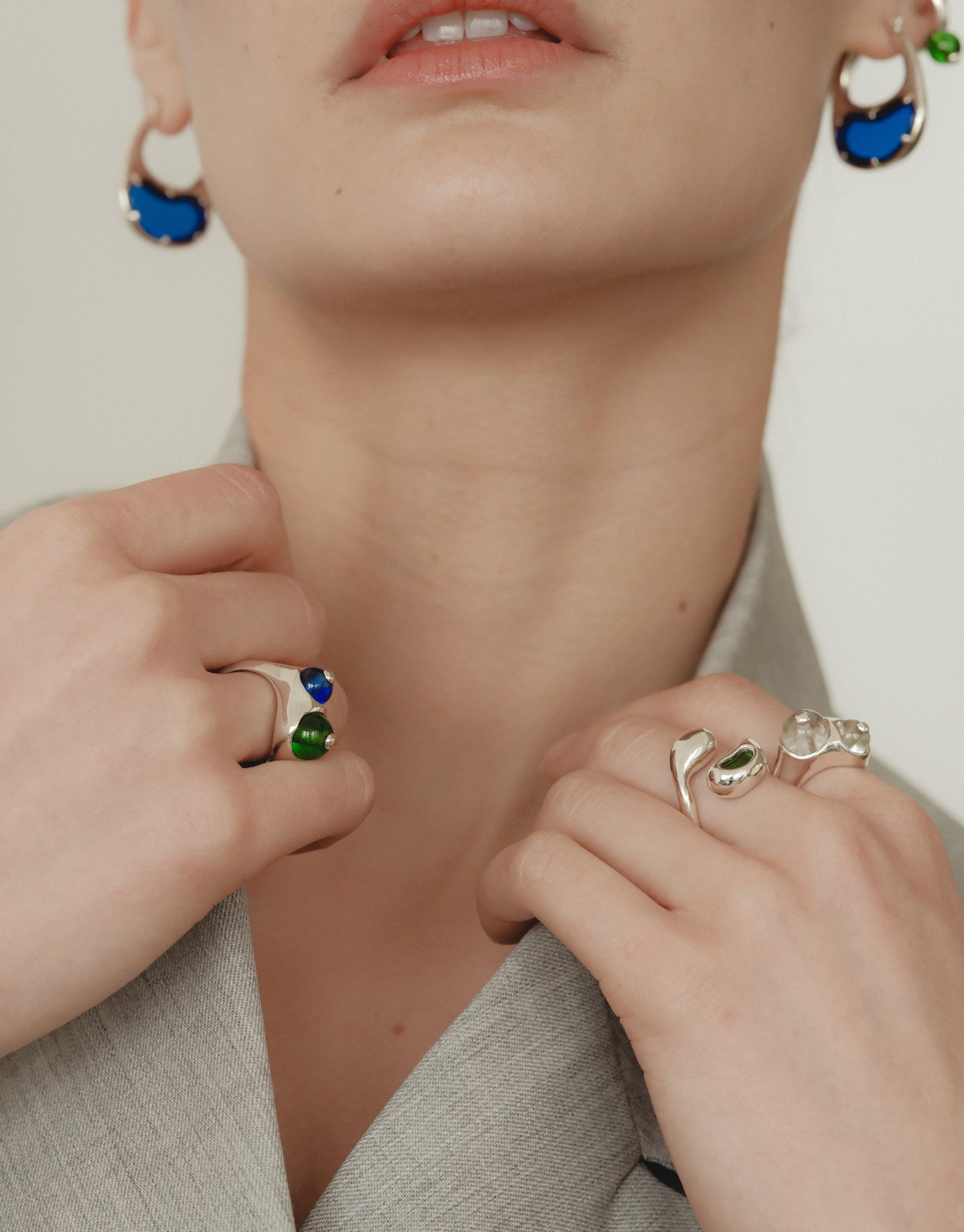 Close-up of hands wearing elegant rings and Bean Hoop Earrings in Large, showcasing nature-inspired jewelry designs. The earrings feature a unique legume-shaped pattern with white and blue elements, capturing the essence of organic transformation. Stylish and creative accessories by CLED.