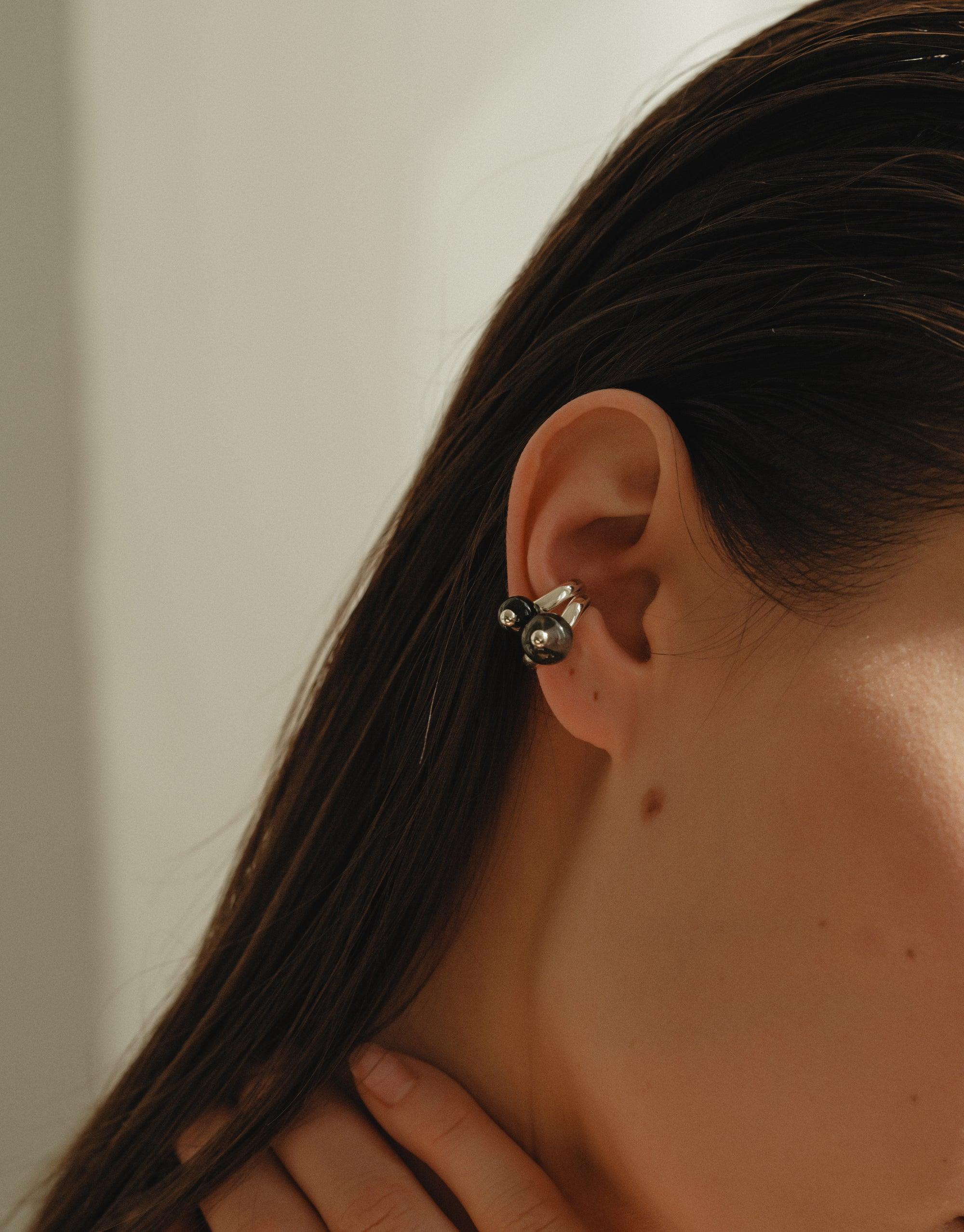 Close-up of a person wearing a small, silver-toned pea-shaped ear cuff. The cuff elegantly wraps around the upper part of the ear, showcasing its unique organic design inspired by nature. Pea Ear Cuff | Small by CLED