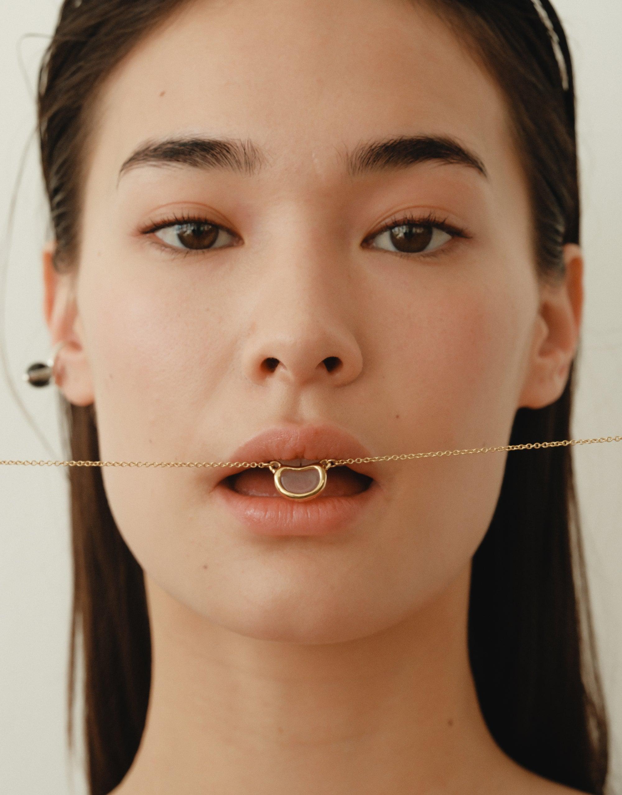 Close-up of model wearing Pea Ear Cuff | Large, showcasing delicate gold chain across lips, highlighting organic shape inspired by nature's creativity. Ear cuff design echoes legume plant's soft curves and intricate patterns, symbolizing growth and transformation. CLED