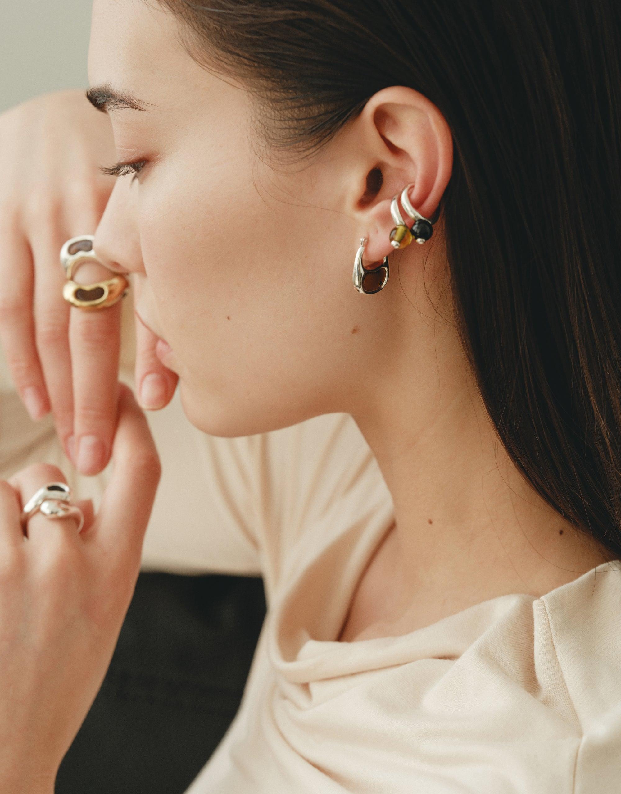 Close-up profile of woman wearing silver ear cuff and multiple rings, showcasing elegant jewelry design inspired by nature. Pea Ear Cuff | Large visible on ear, exemplifying organic shapes and curves reminiscent of legume plants. Stylish and transformative accessory by CLED.