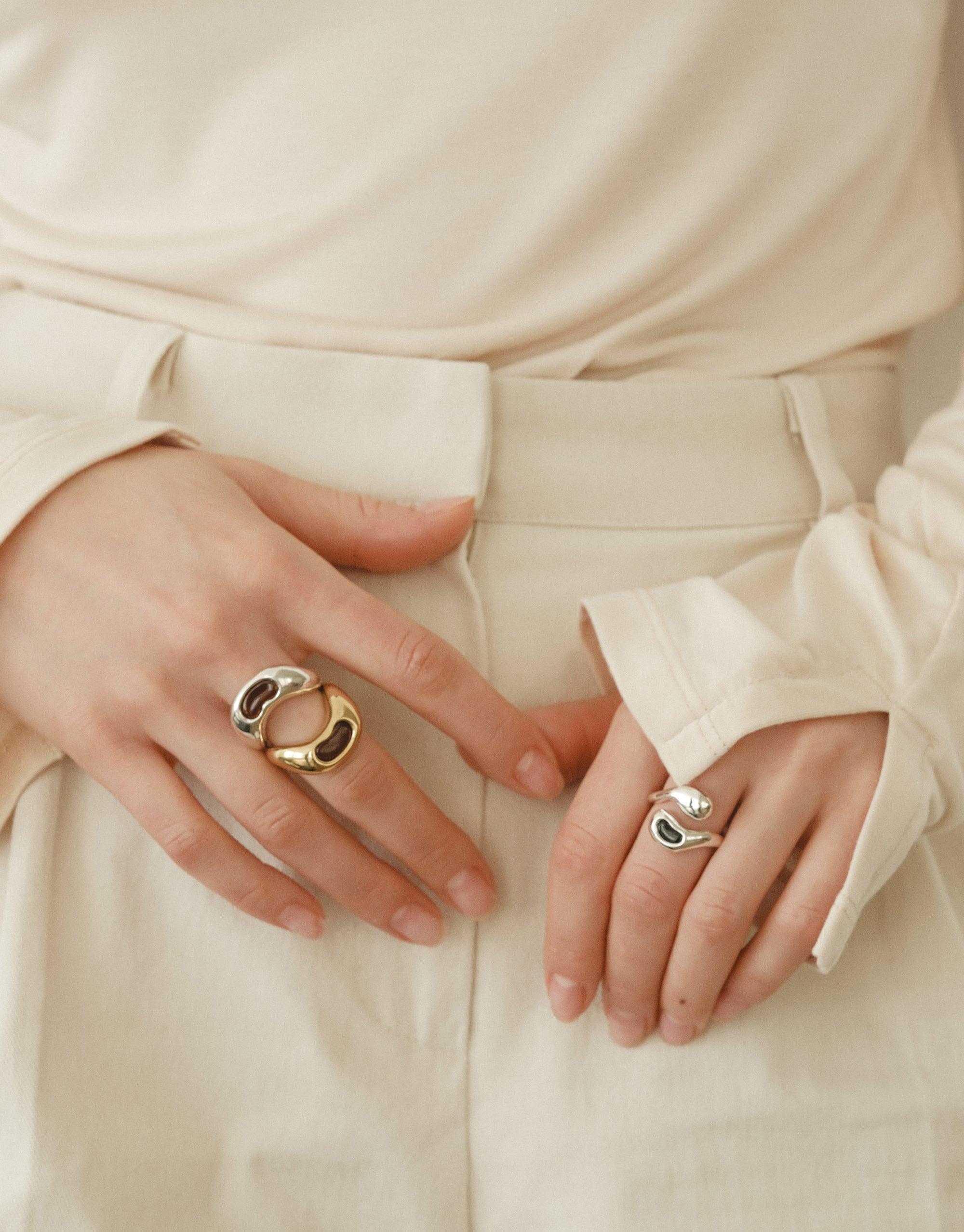 Close-up of hands wearing unique gold and silver Bean Ring, inspired by organic legume shapes. Elegant jewelry showcasing nature-inspired design against neutral brown top. Stylish and sophisticated accessory for the modern woman. Bean Ring by CLED.