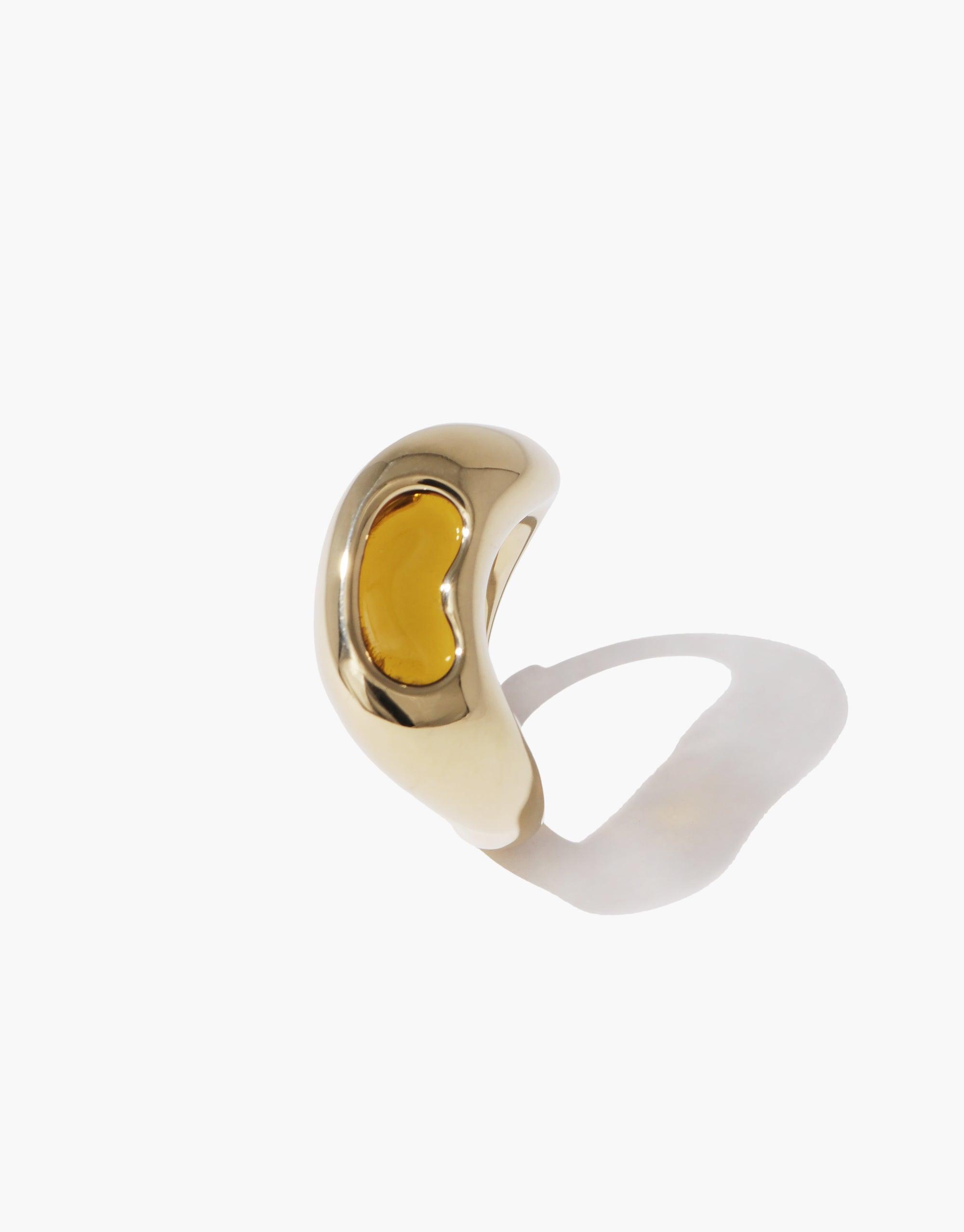 Elegant gold-toned Bean Ring with smooth curved shape and yellow accent, inspired by nature's organic forms. Unique jewelry piece reflecting growth and transformation. Stylish accessory for contemporary fashion enthusiasts. CLED Bean Ring