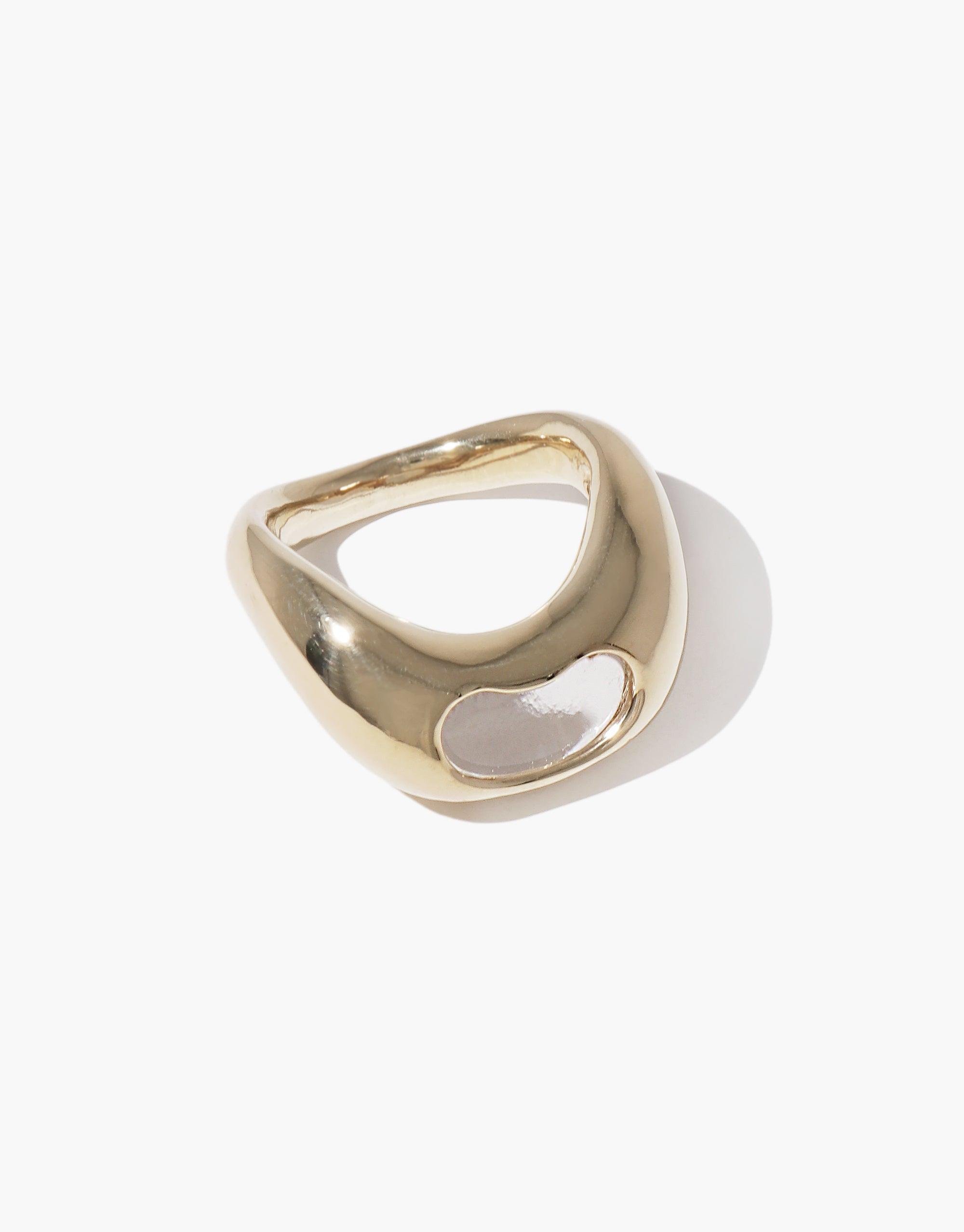 Elegant gold-toned Bean Ring with organic curved shape, inspired by legume plants. Smooth metallic surface with a small white accent, symbolizing growth and nature's creativity. Unique jewelry piece reflecting natural beauty and transformation. CLED Bean Ring.