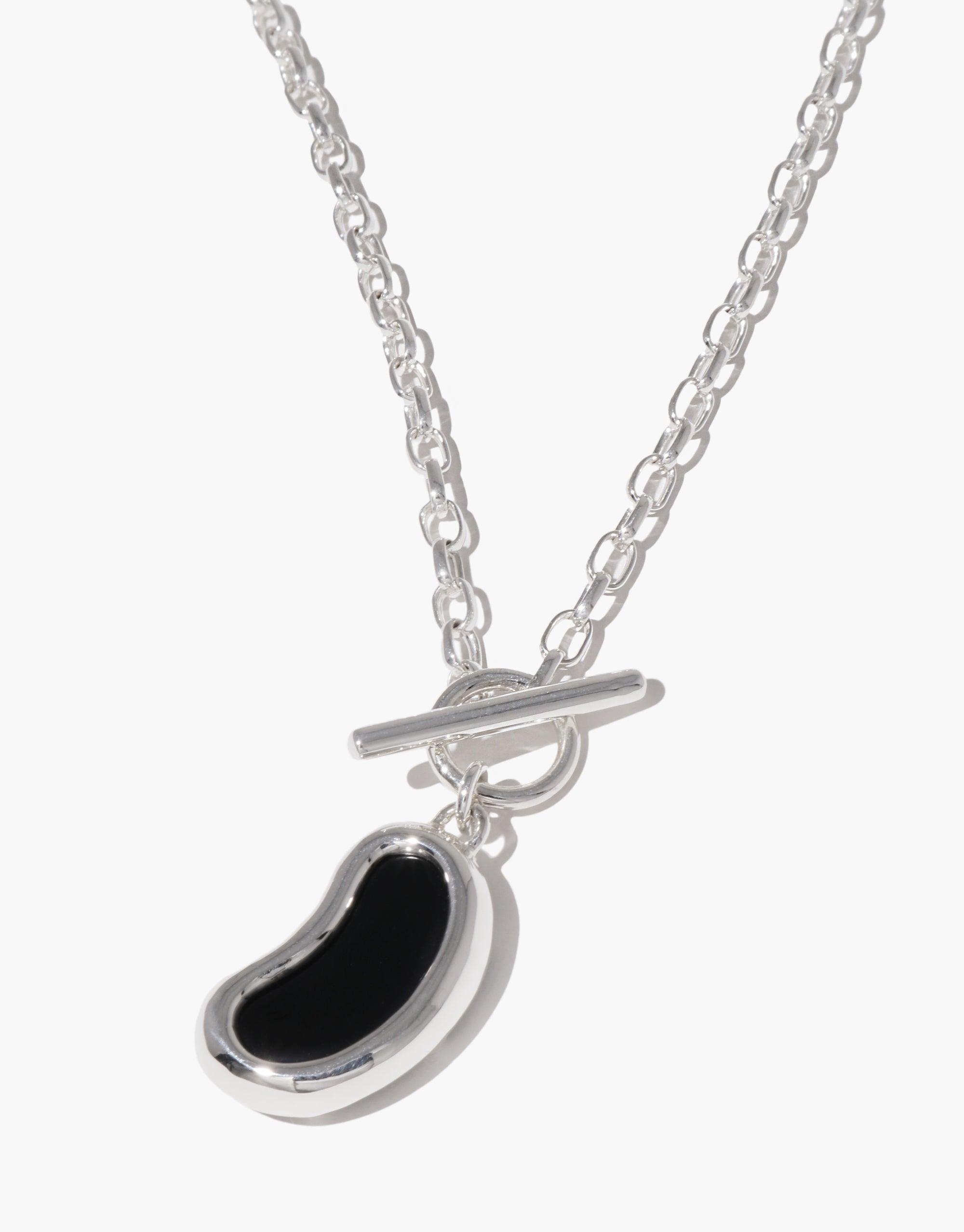 Silver chain necklace with black bean-shaped pendant, inspired by organic legume forms. Toggle clasp closure. Bean Toggle Necklace showcases nature-inspired jewelry design. CLED