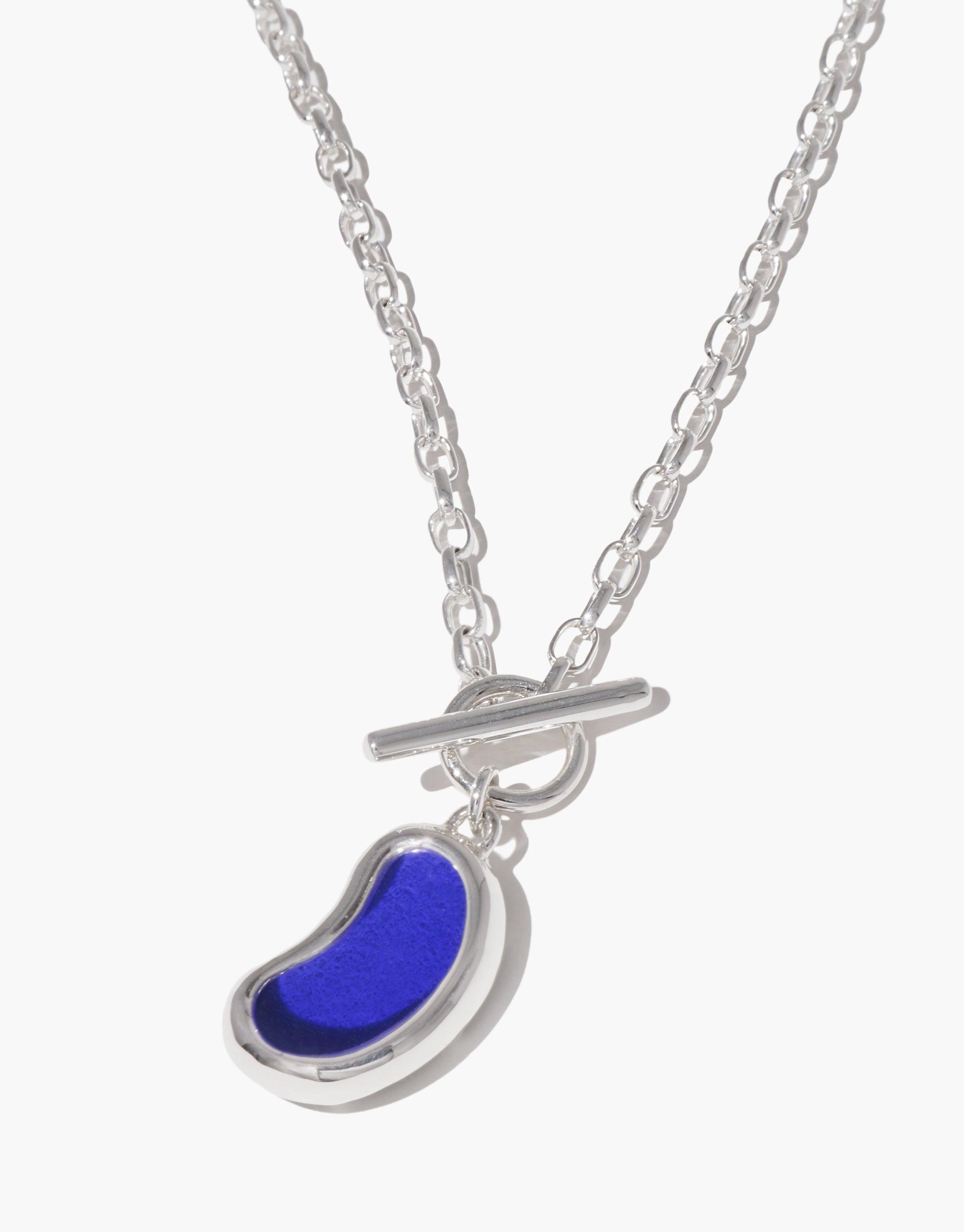 Bean Toggle Necklace featuring a silver chain with a vibrant blue bean-shaped pendant. The necklace showcases a unique toggle clasp, embodying nature-inspired elegance. A striking accessory that captures the organic beauty of legumes, perfect for everyday wear. CLED Bean Toggle Necklace.