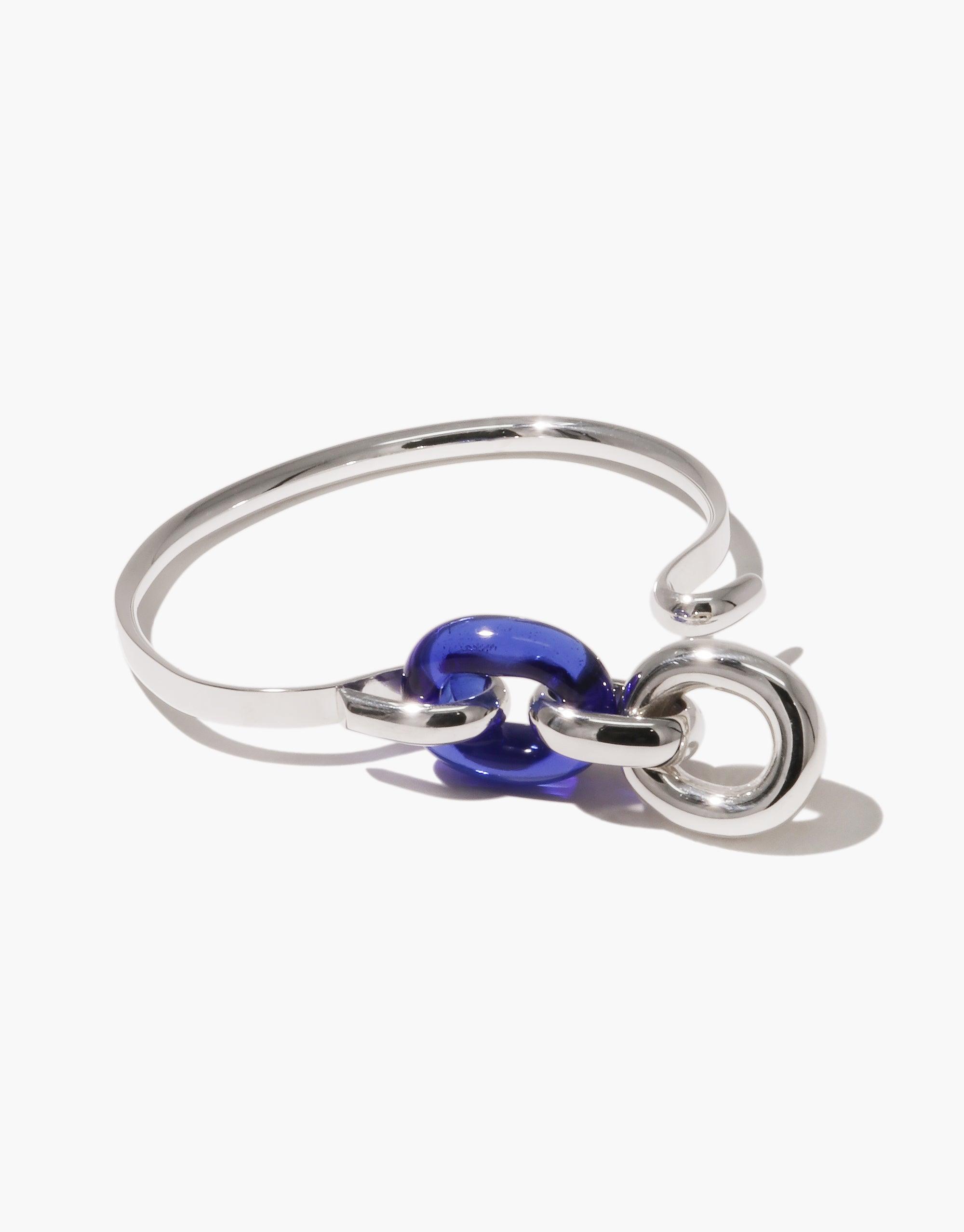 Sleek silver bracelet with blue glass link, showcasing modern design and upcycled materials. Loop Hook Bracelet features an open-ended style, symbolizing unity and sustainability. Elegant accessory from the In The Loop collection by CLED.