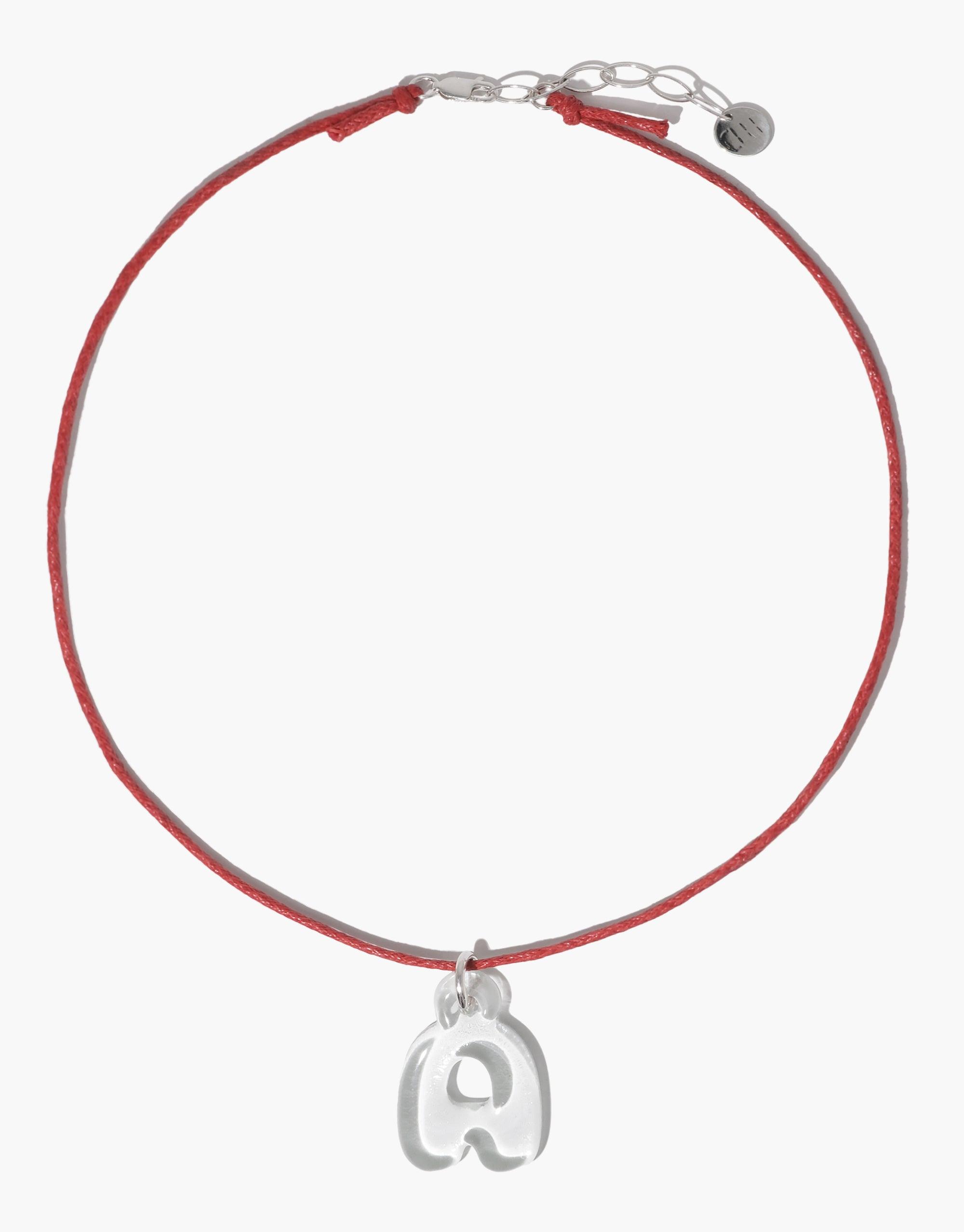 Red cotton cord necklace with adjustable silver clasp and small letter 'A' charm pendant. Versatile accessory for layering or solo wear. Minimalist design perfect for customization with additional charms. Cord Necklace by CLED.
