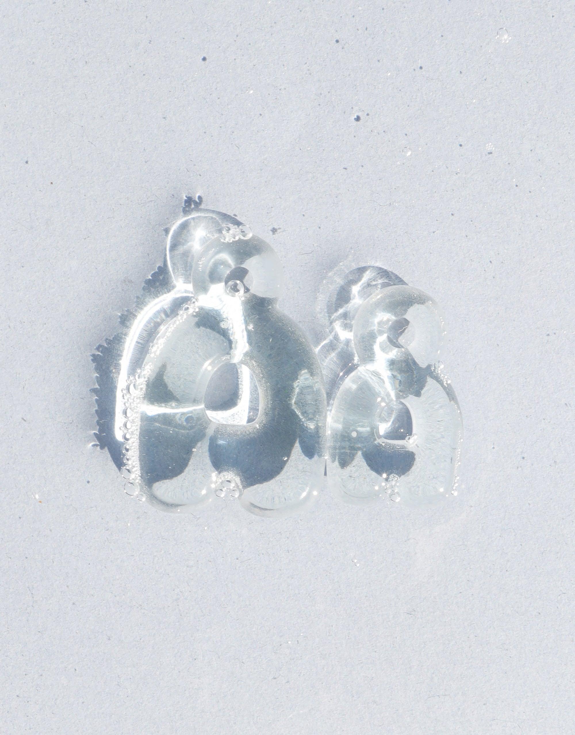 Transparent bubble-like letter charms 'C' and 'D' on a light background, showcasing the rounded, playful design of the Letter Charm | Alphabet product. Eco-friendly glass jewelry that transforms discarded materials into stylish accessories. CLED