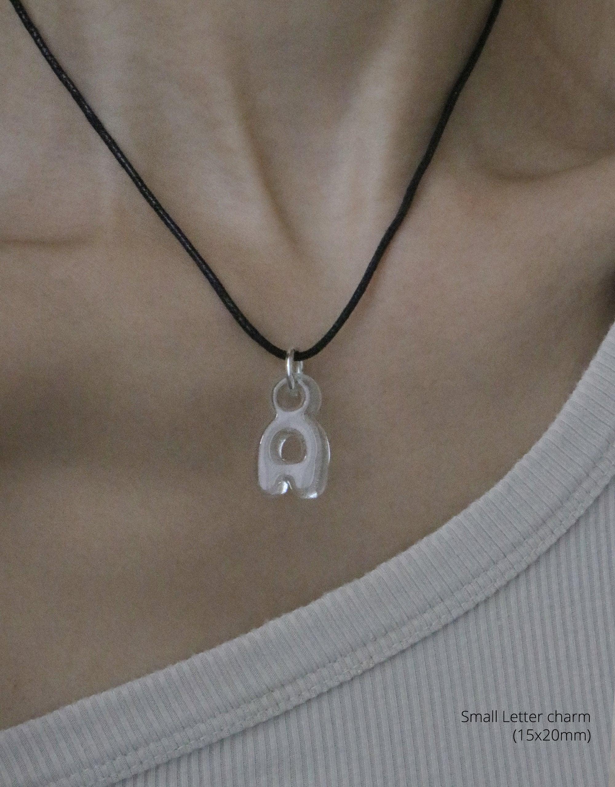 Eco-friendly bubble letter 'a' charm necklace on black cord, showcasing recycled glass pendant with soft, rounded form. Versatile accessory for personal expression. Letter Charm | Alphabet by CLED