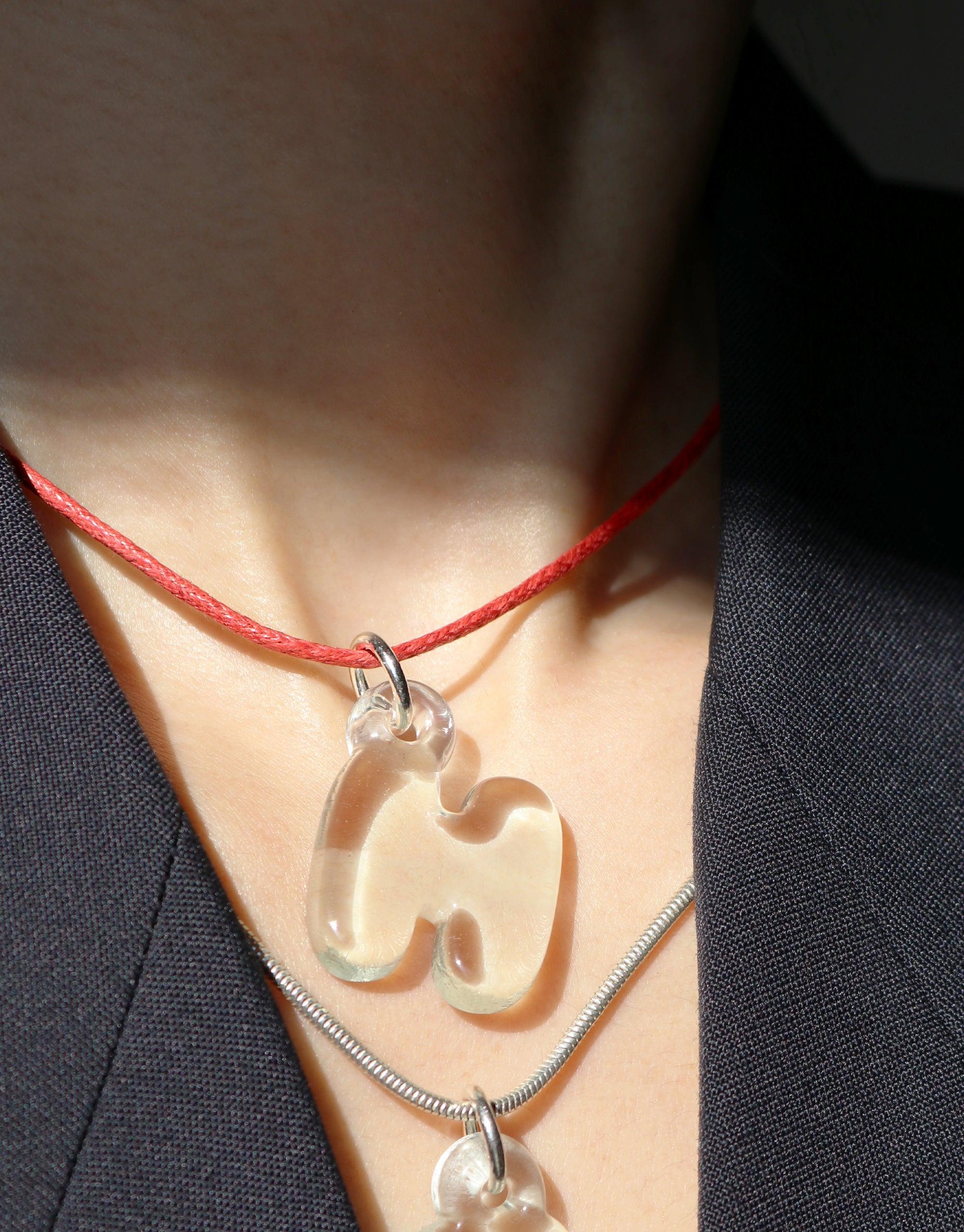 Close-up of a delicate red cord necklace with a transparent charm and a silver Snake Chain Necklace layered beneath, worn against skin and dark clothing. Versatile and stylish accessory for customizable charm combinations. Snake Chain Necklace by CLED.