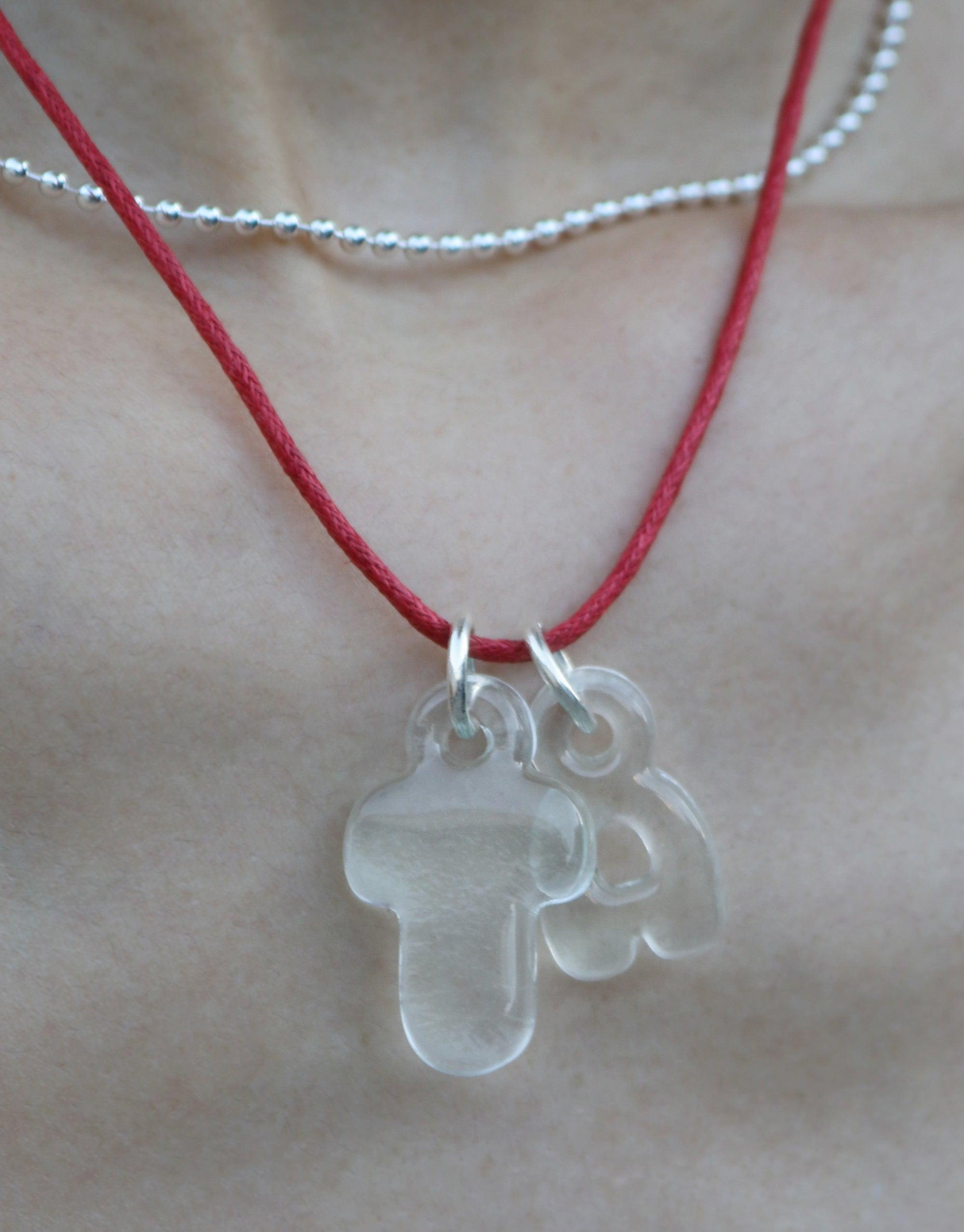 Eco-friendly bubble letter charms on red cord necklace, showcasing recycled glass alphabet pendants. Transparent, rounded letters for personalized expression. Layered with delicate silver chain. Sustainable jewelry by CLED. Letter Charm | Alphabet.