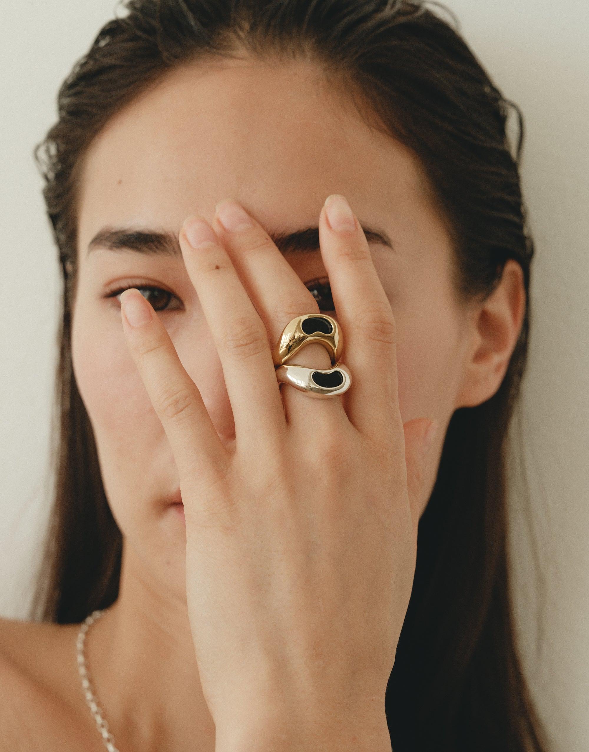 Elegant Bean Ring showcasing organic curves and nature-inspired design, worn on a woman's hand covering part of her face, highlighting the ring's unique shape and artistic appeal. Sustainable jewelry embodying growth and transformation. CLED Bean Ring