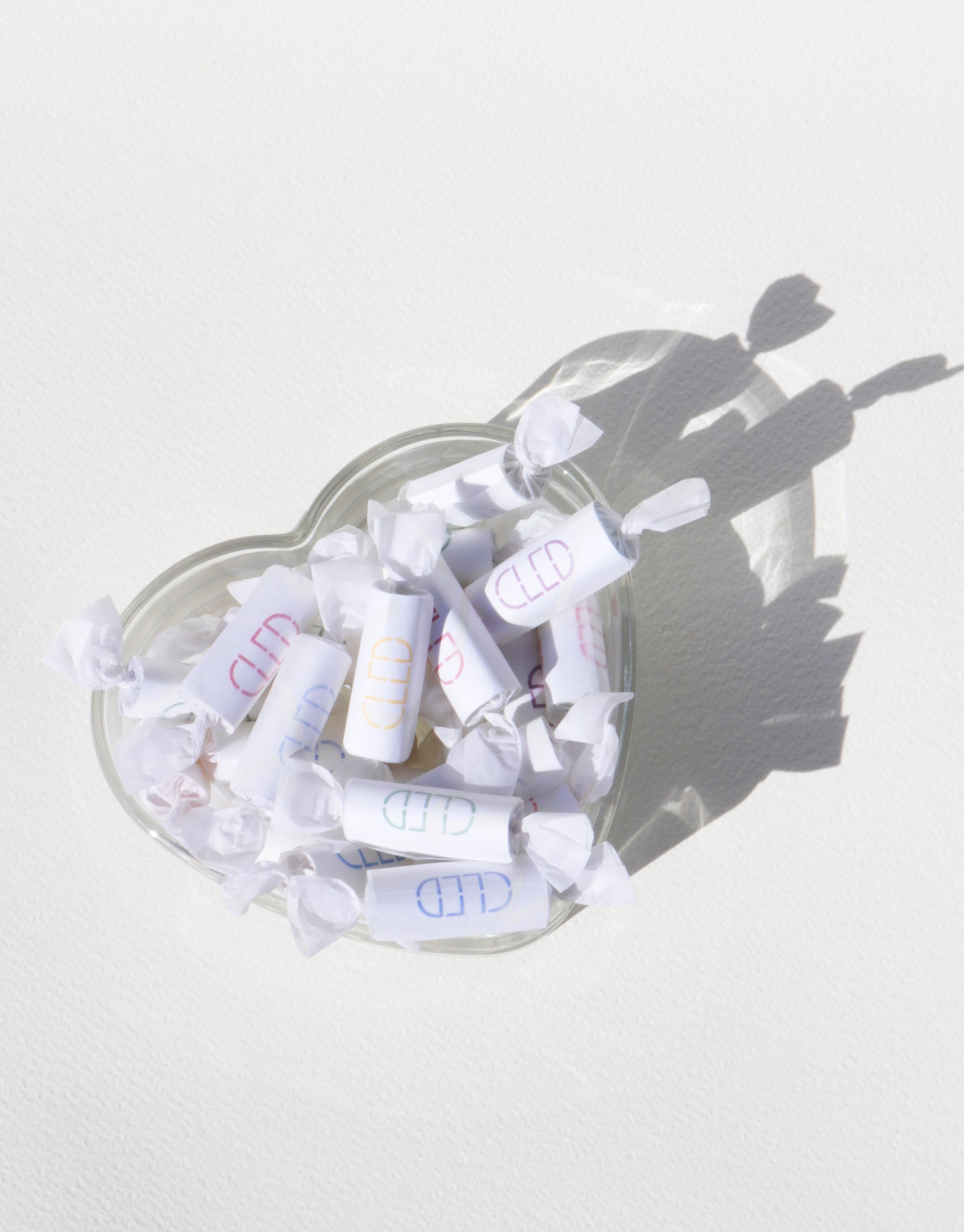 A heart-shaped bowl filled with assorted candies, casting the shadow of an individual nearby.
