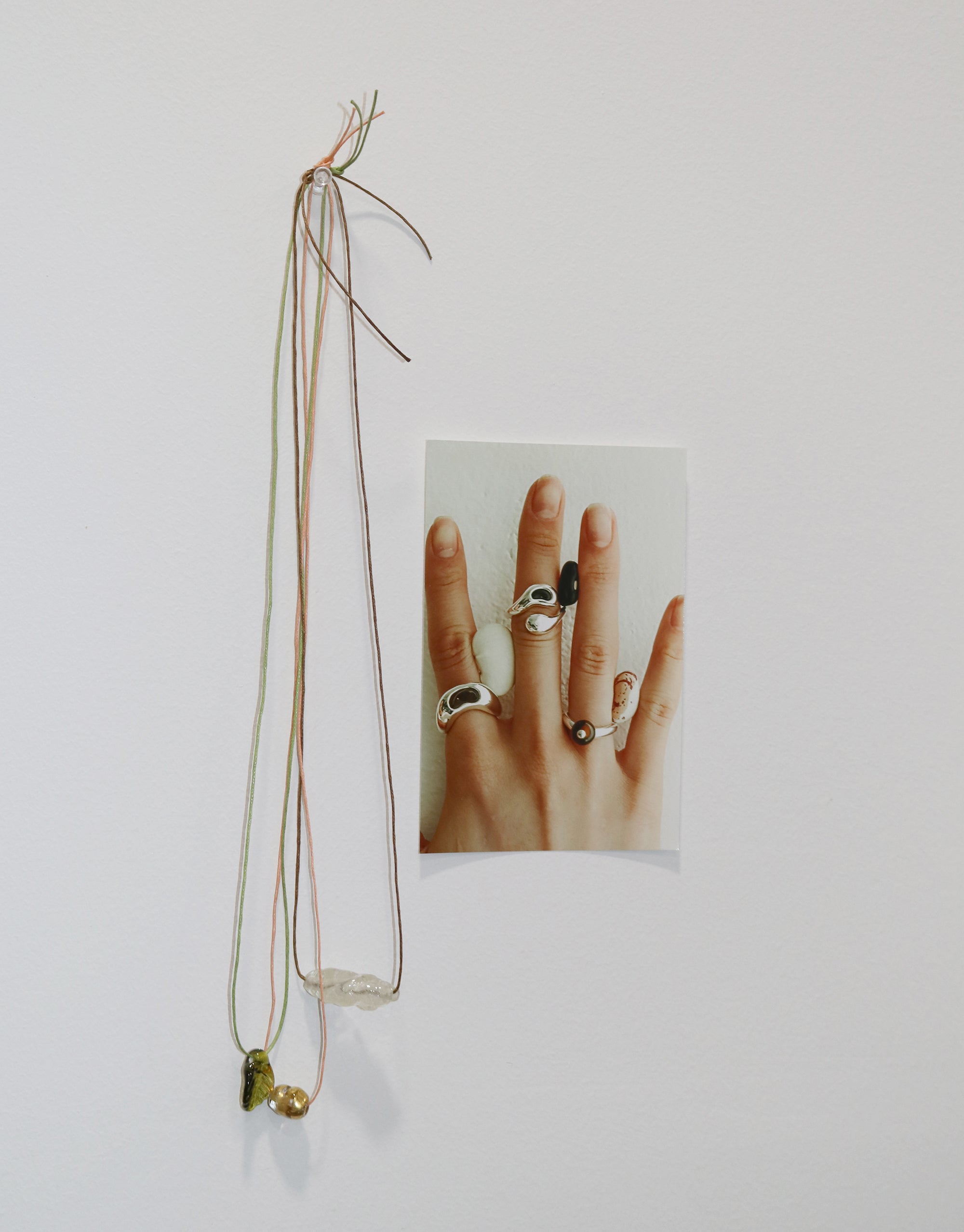 A wall displays an image of a hand with multiple rings and a set of necklaces hanging beside it.