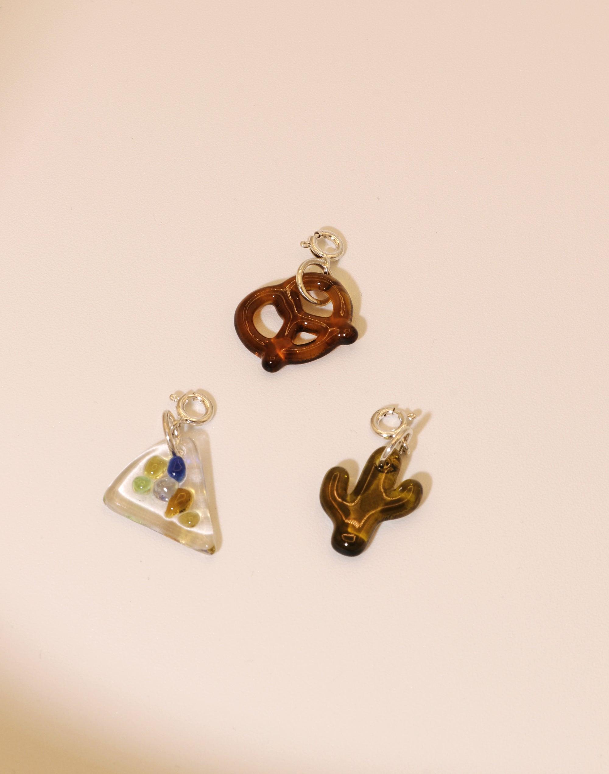 Handmade upcycled glass charms featuring pretzel, pizza slice, and cactus shapes for necklaces or bracelets. Eco-friendly jewelry accessories in warm amber and clear tones. Pizza | Icon Charm by CLED