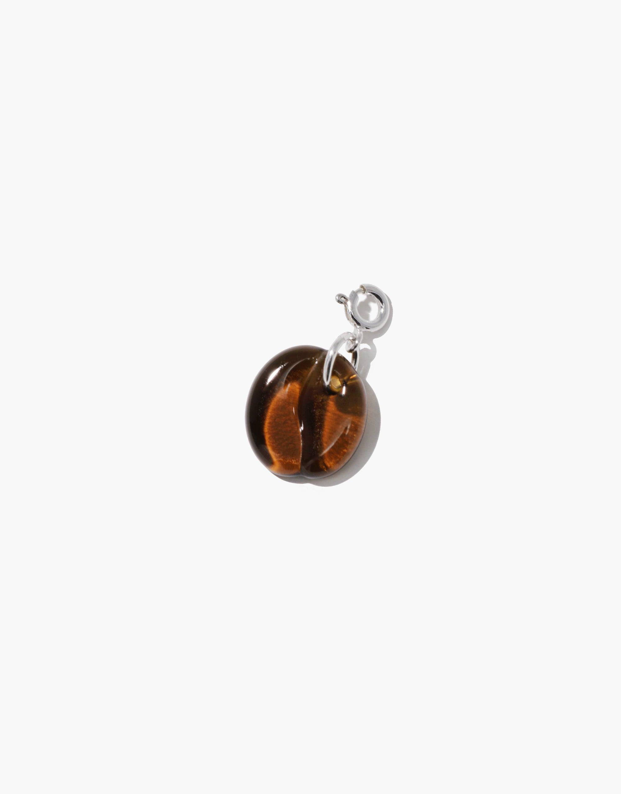 Coffee Bean Icon Charm featuring a small, transparent brown spherical pendant with a silver-toned clasp, perfect for adding a playful touch to necklaces or bracelets. This quirky accessory showcases the iconic shape of a coffee bean, ideal for coffee lovers. CLED