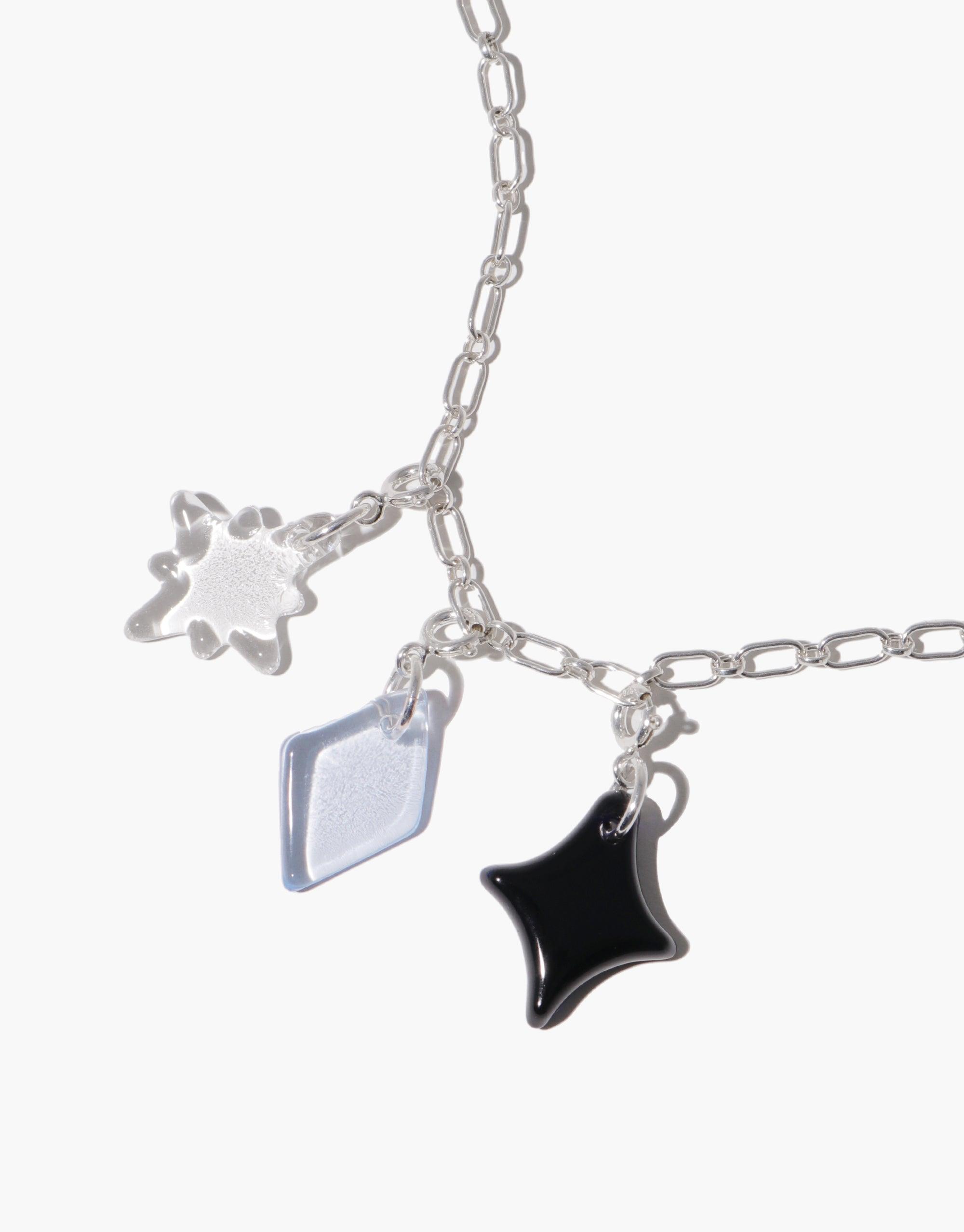 Silver chain necklace with three hanging charms: a star-shaped charm, a diamond-shaped charm, and a four-pointed star-shaped charm in black. Sparkle A | Icon Charm showcases playful shapes for stylish accessorizing. CLED