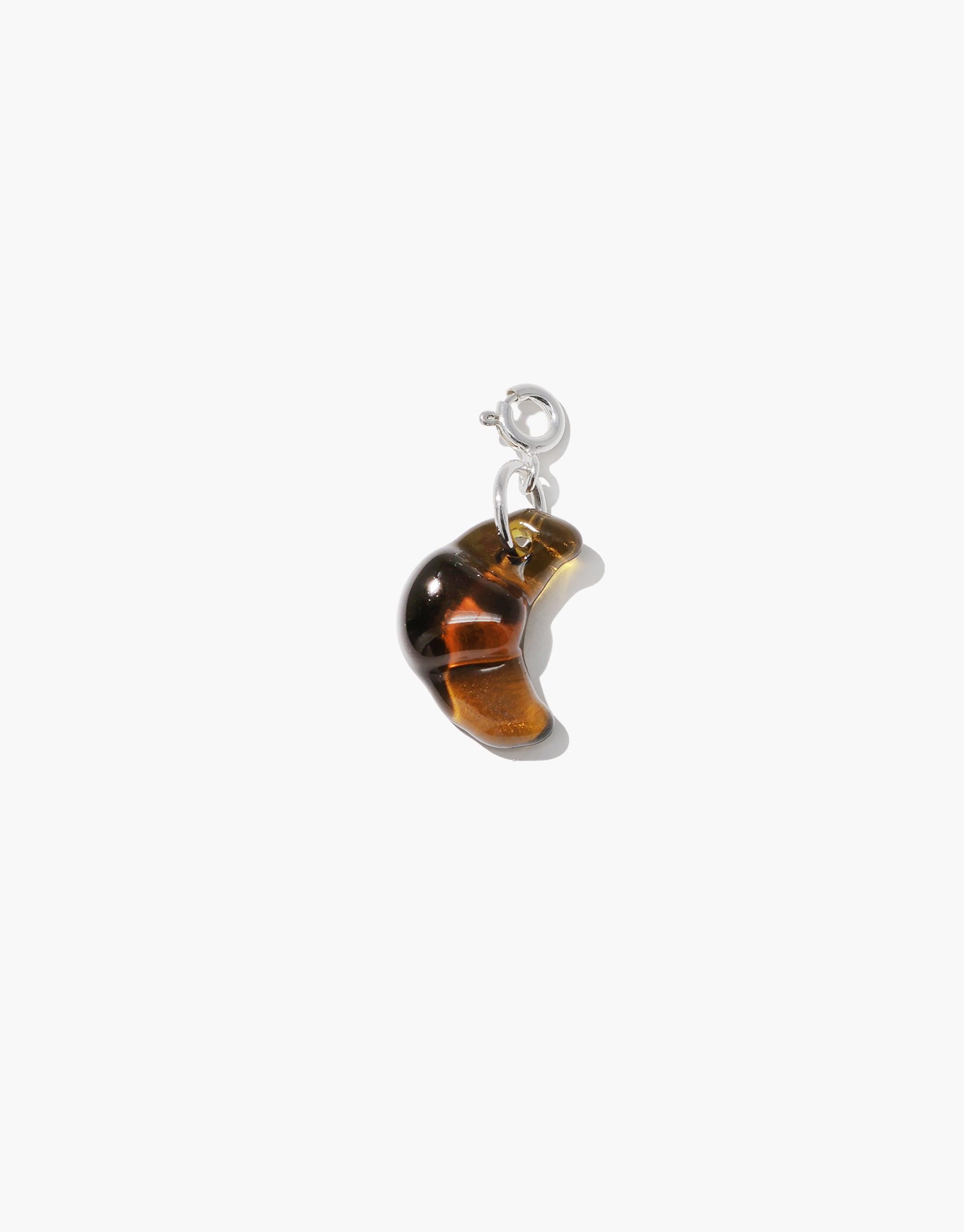 Croissant-shaped amber-colored charm pendant with silver attachment, perfect for adding a playful and quirky touch to necklaces or bracelets. Croissant | Icon Charm by CLED