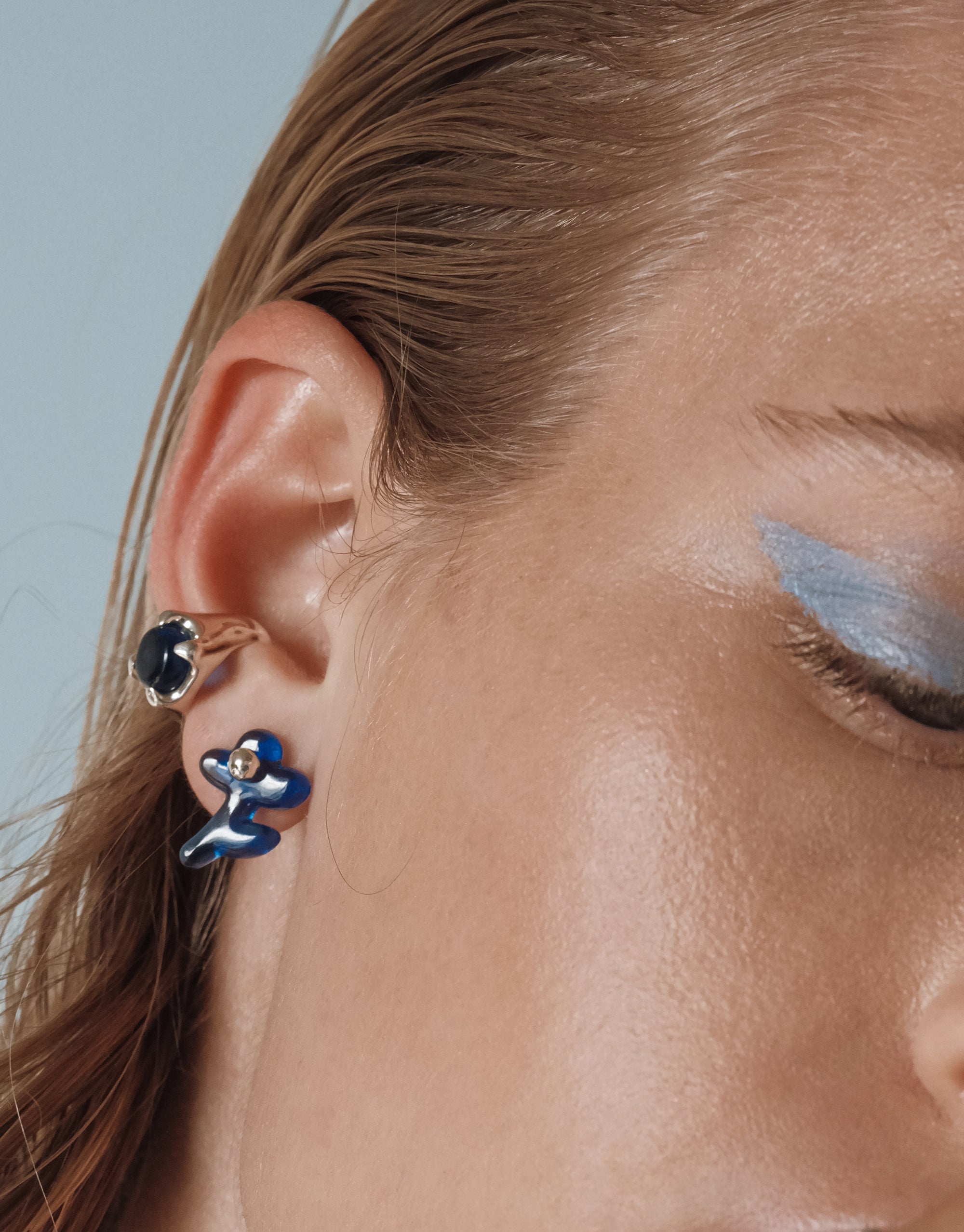 Mismatched Petal Icon Stud Earrings with blue floral design and silver studs shown on ear, sculptural modern style by CLED