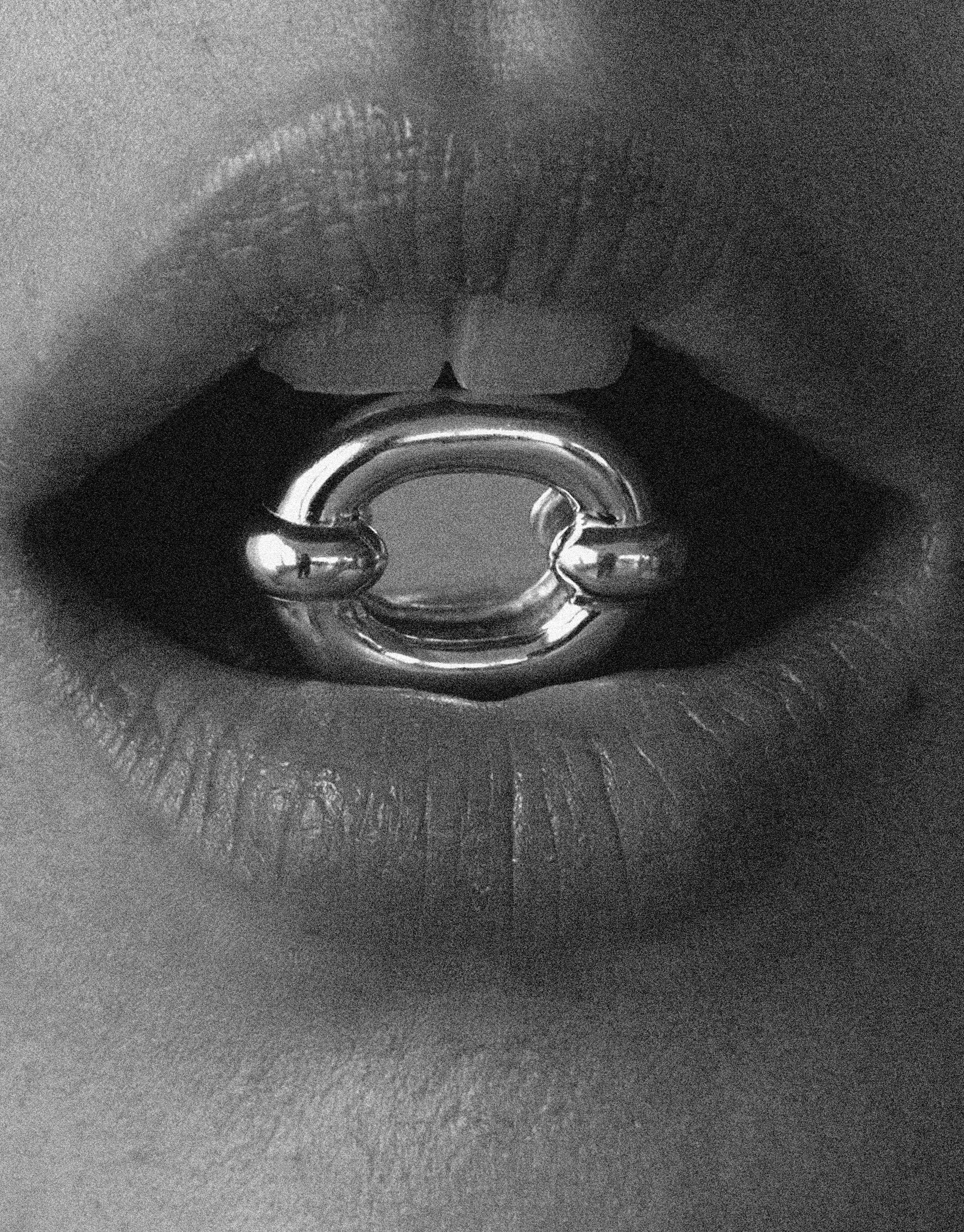 Close-up black and white image of lips wearing the Core Loop Ring | Large, showcasing its sleek metal design with a reflective center. Elegant and modern jewelry piece by CLED.