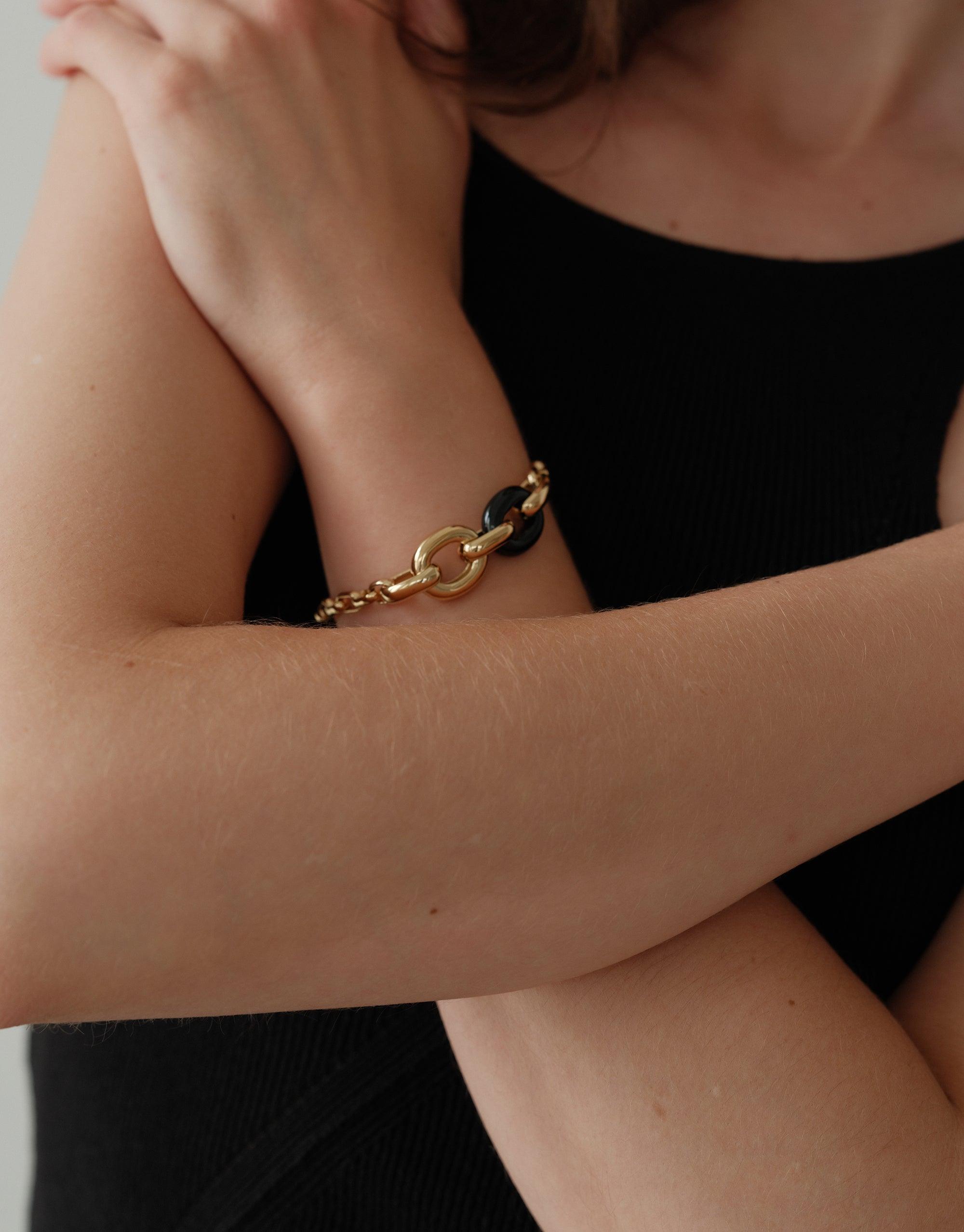 Elegant Loop Chain Bracelet featuring gold and black links, worn on wrist against black top. Showcases sustainable design and upcycled materials. Symbolizes unity and connection from CLED's In The Loop collection. Loop Chain Bracelet by CLED.