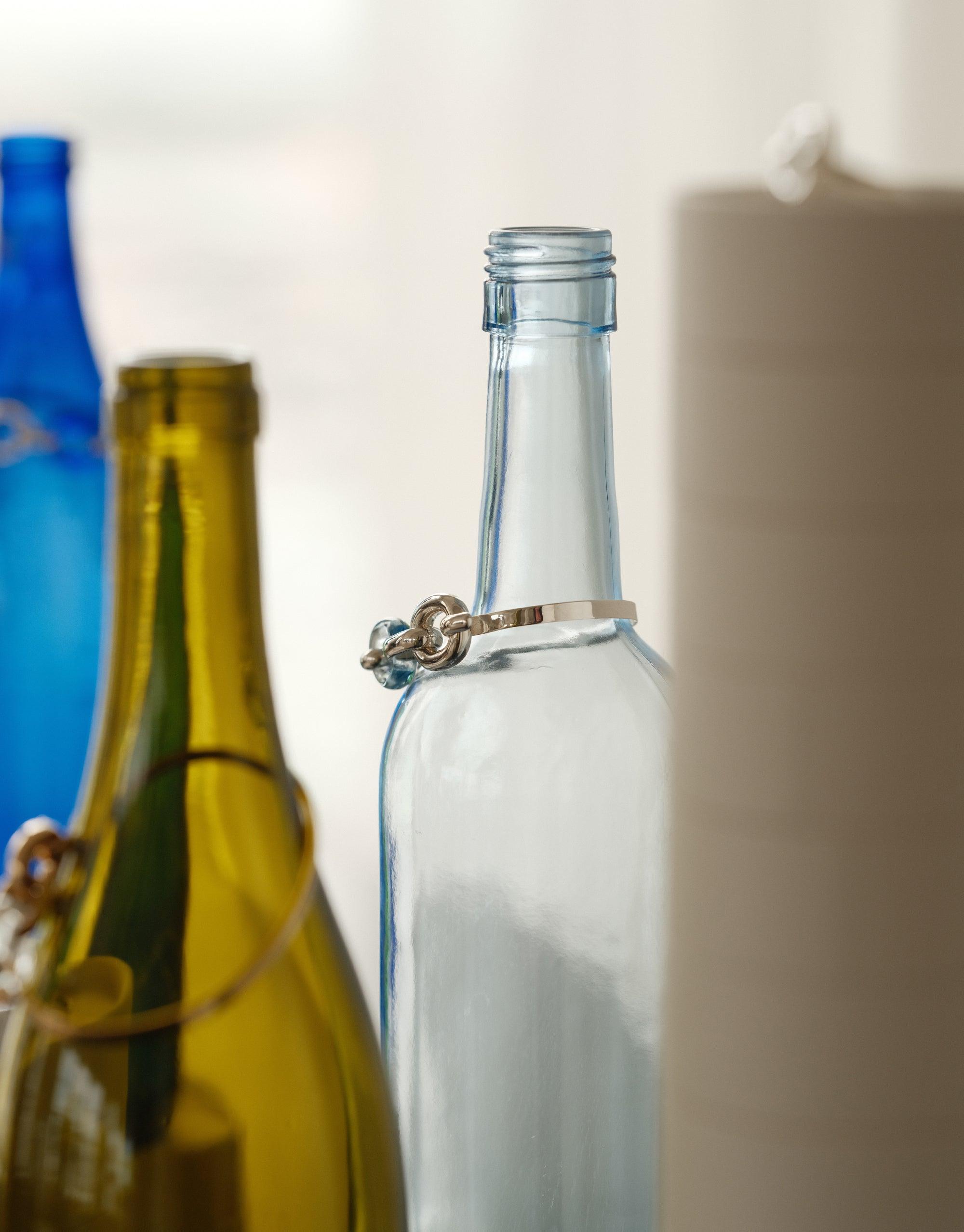 Loop Hook Bracelet elegantly displayed on a glass bottle, showcasing its unique design. Surrounded by colorful upcycled bottles, the bracelet embodies sustainable luxury. A testament to CLED's commitment to transforming discarded materials into treasured accessories. Loop Hook Bracelet by CLED.