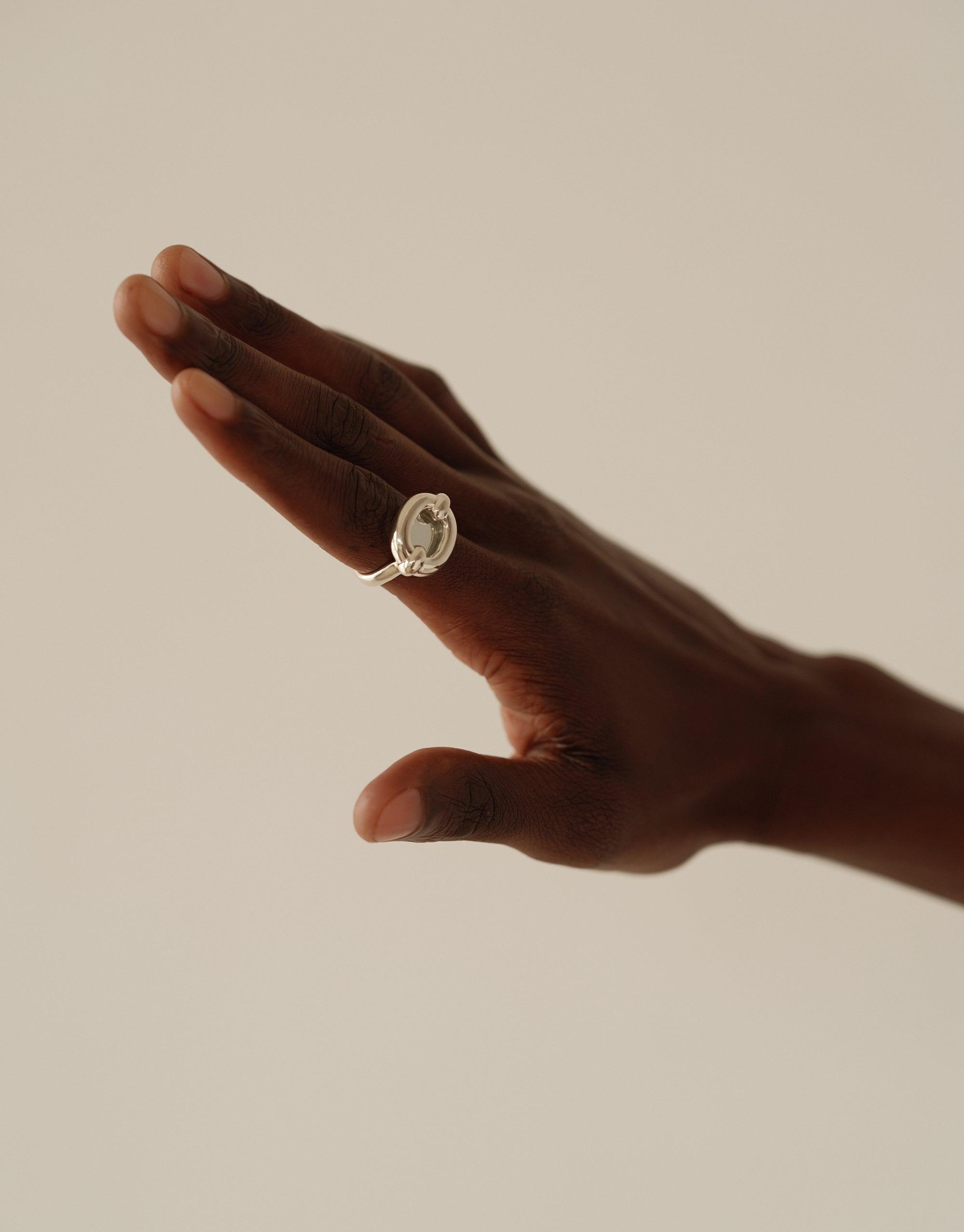 Hand wearing the Core Loop Ring | Large, showcasing its unique design with a seamless eco gem setting. The ring's mirror-like surface reflects light, demonstrating its functional and aesthetic qualities. Elegant and sustainable jewelry piece by CLED.