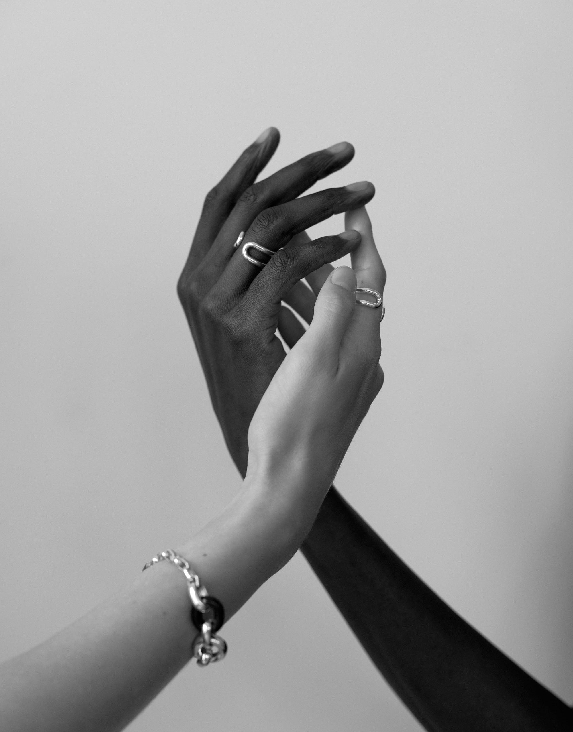 Elegant black and white image of two hands intertwined, showcasing the Infinite Loop Ring. The ring symbolizes unity and connection, reflecting the In The Loop collection's ethos. A powerful representation of togetherness and upcycling philosophy. Infinite Loop Ring by CLED.