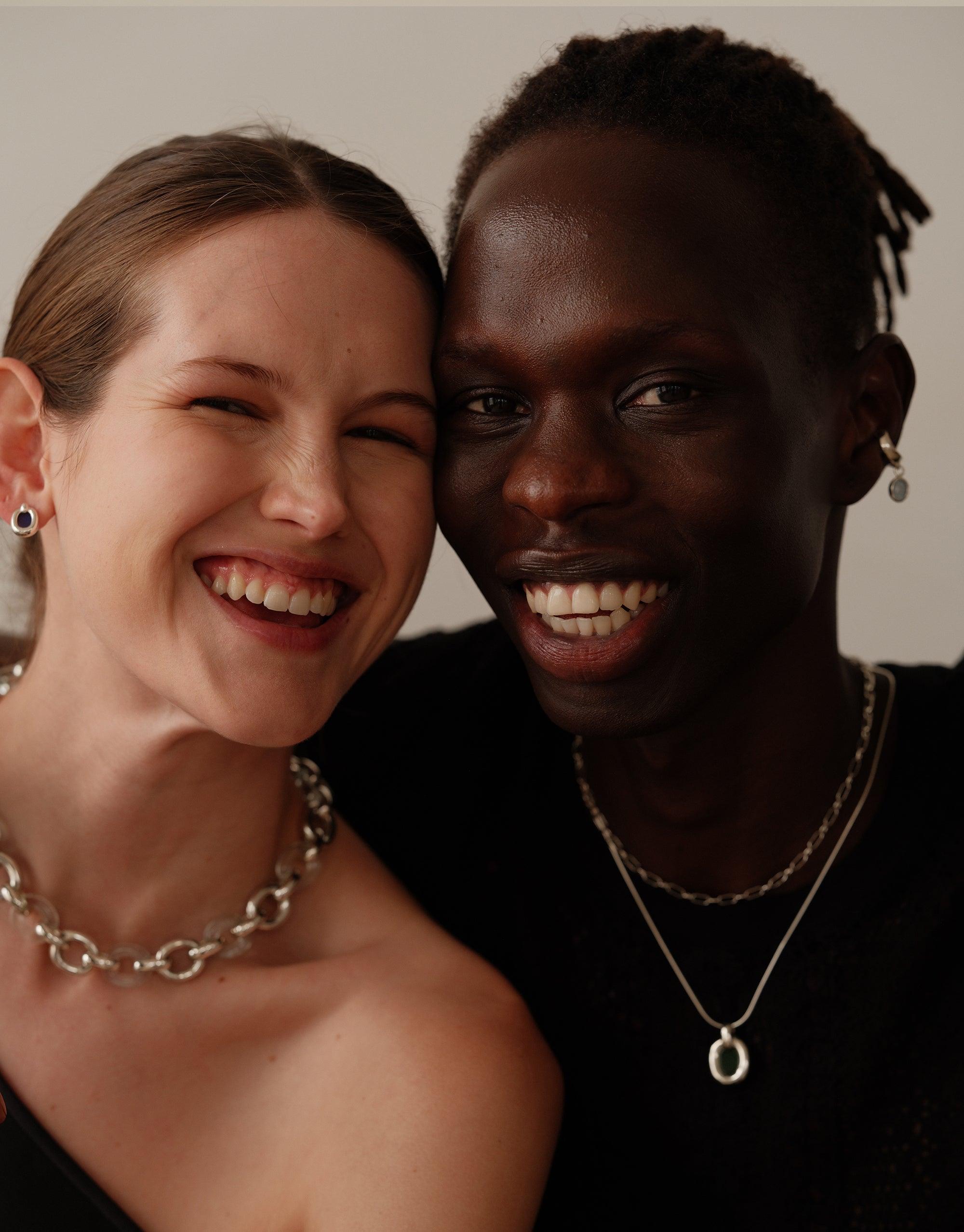 Close-up of two smiling individuals wearing stylish necklaces. The image showcases the Core Loop Necklace and Snake Chain, highlighting the versatility and unifying design of CLED's Loop Collection jewelry pieces.