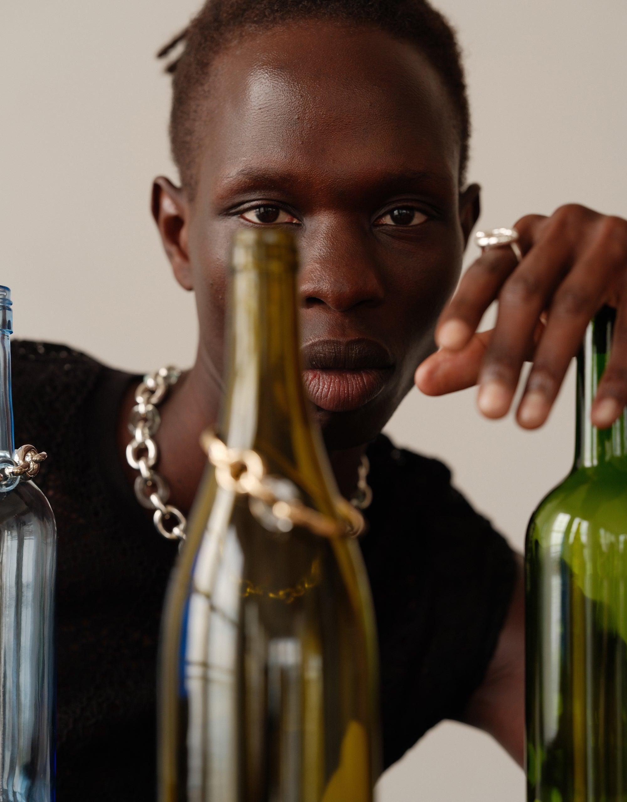 Close-up image showcasing upcycled Loop Hook Bracelet among colorful glass bottles, demonstrating CLED's commitment to sustainable fashion and unity. Stylish accessory from the In The Loop collection by CLED.
