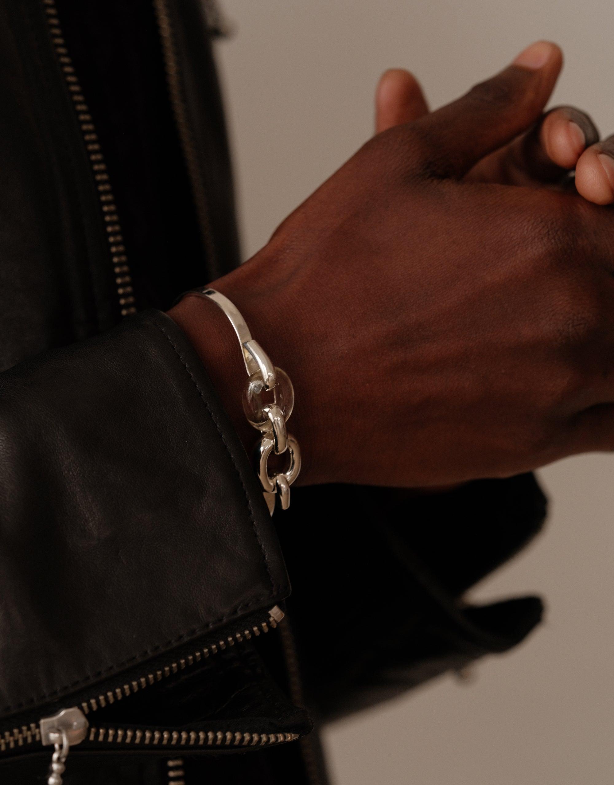 Stylish silver Loop Hook Bracelet worn on wrist, showcasing intricate chain design against black leather jacket. Symbolizes unity and upcycling ethos. Elegant accessory for conscious fashion lovers. CLED Loop Hook Bracelet.