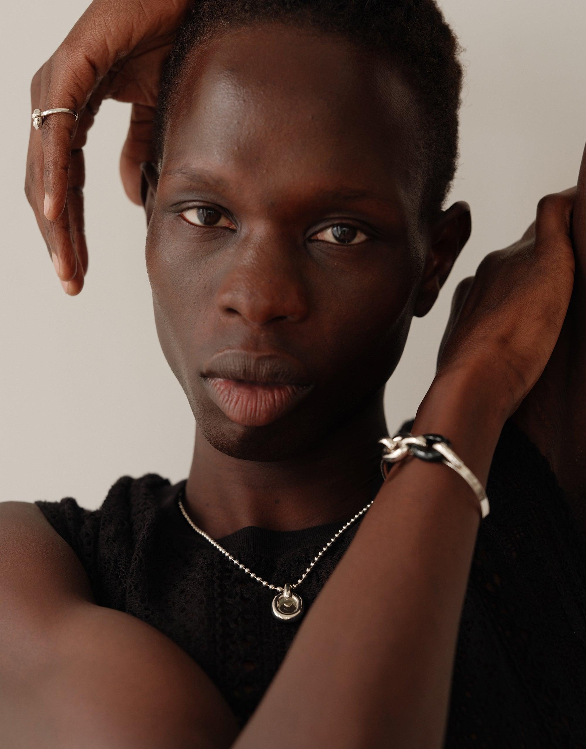 Close-up portrait showcasing the Core Loop Necklace | Ball Chain, a sleek silver necklace with a circular pendant. The model wears a black top, emphasizing the necklace's elegant design. The image highlights the necklace's versatility and connection to CLED's upcycling mission.