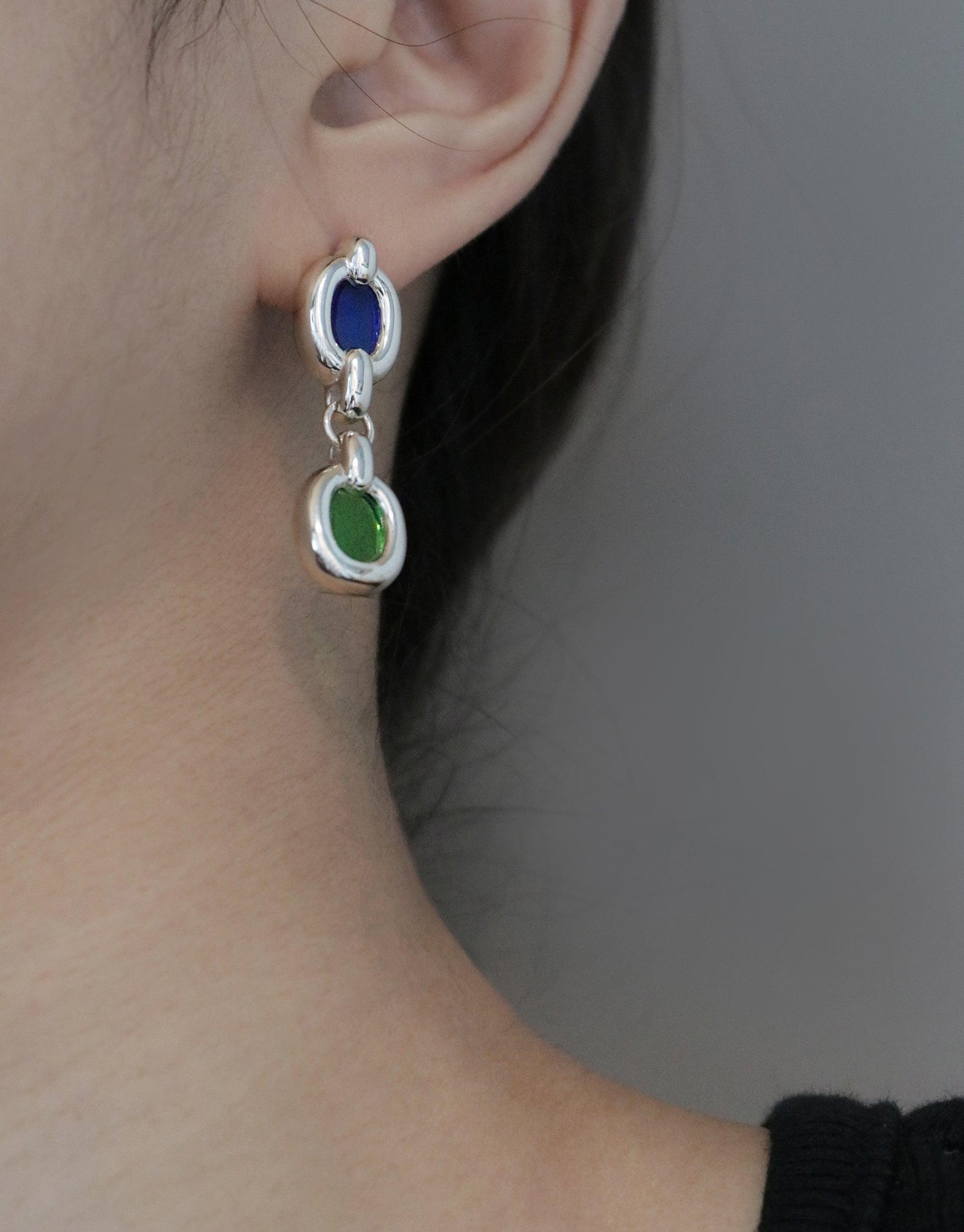 Duo Core Loop Earrings featuring silver-toned metal with blue and green upcycled elements, showcasing sustainable design. Elegant drop style earring worn on an ear, symbolizing unity and connection. Part of the In The Loop collection by CLED.