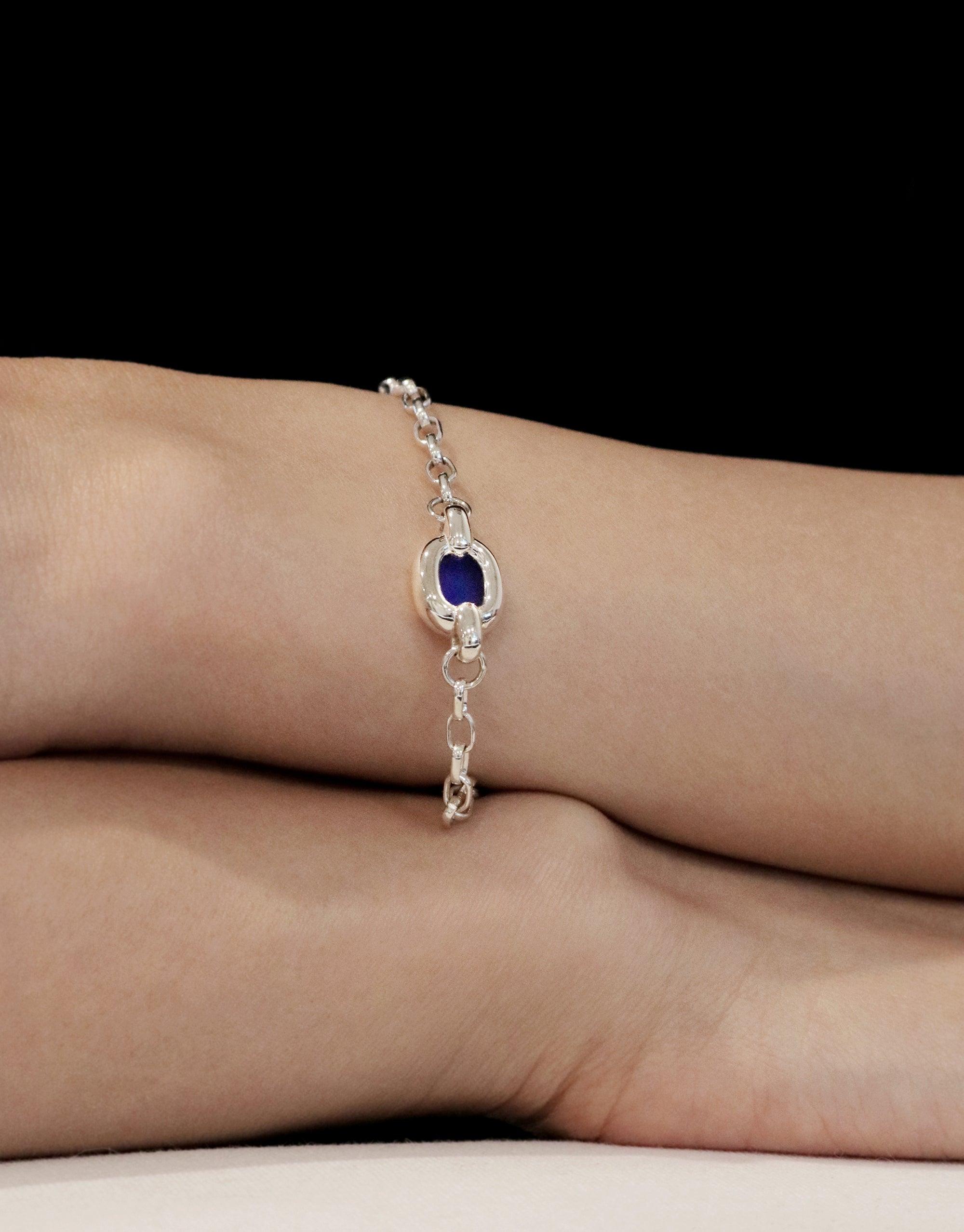 Elegant Core Loop Bracelet featuring a delicate silver chain with a central blue stone accent, showcasing upcycled design and unity symbolism. Worn on a model's wrist against a dark background, embodying sustainable luxury. CLED Core Loop Bracelet.