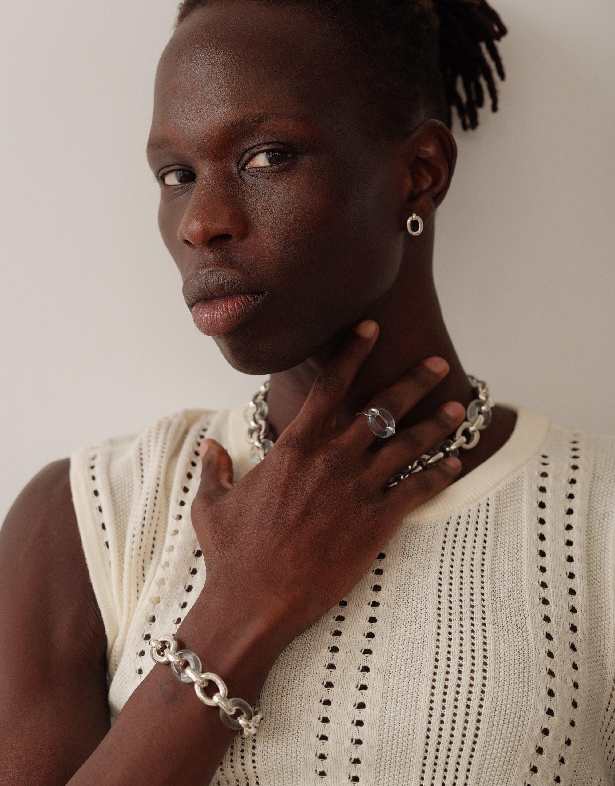 Model wearing Connected Loop Bracelet in mixed metal and glass, paired with matching necklace and ring. Sleeveless cream top with eyelet detailing. Showcases upcycled jewelry design that symbolizes unity and connection. Connected Loop Bracelet | Mixed Metal & Glass CLED